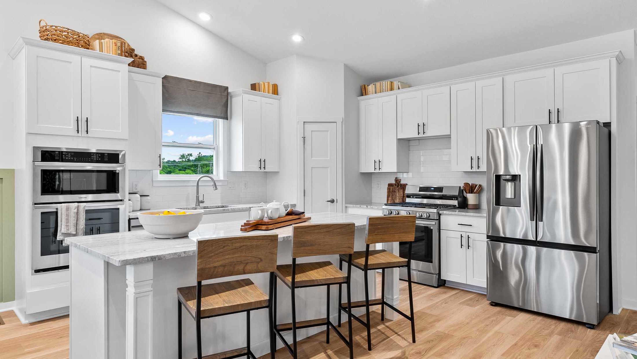 Modern kitchen with stainless steel appliances, white cabinetry, and a central island with wooden stools.