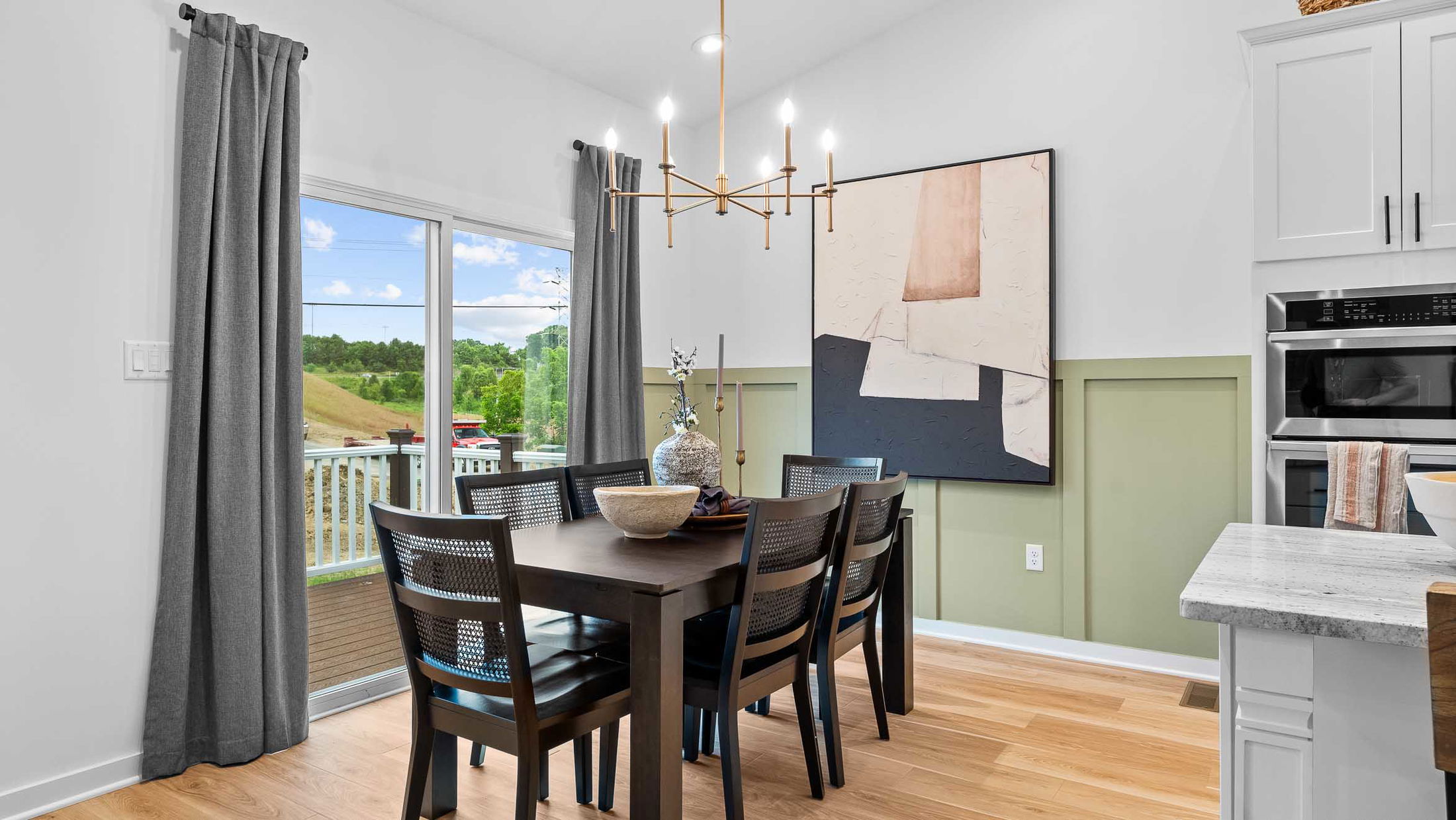 Modern dining room with a dark wood table, abstract wall art, and a view of a green landscape through a sliding glass door.