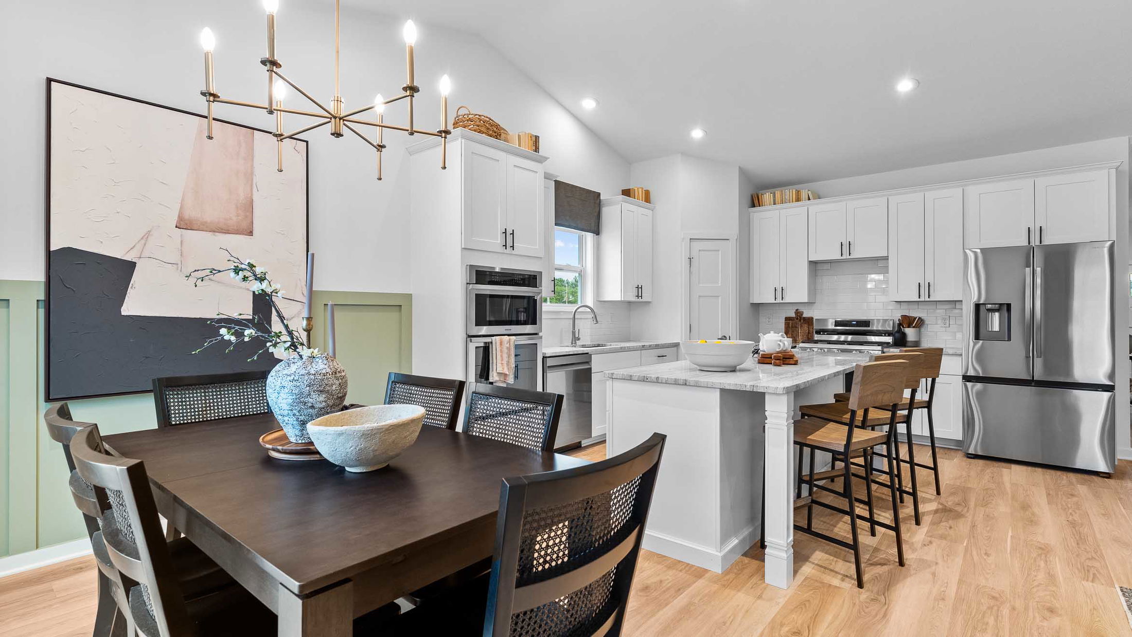 Modern kitchen and dining area with stainless steel appliances, white cabinets, and wooden accents.