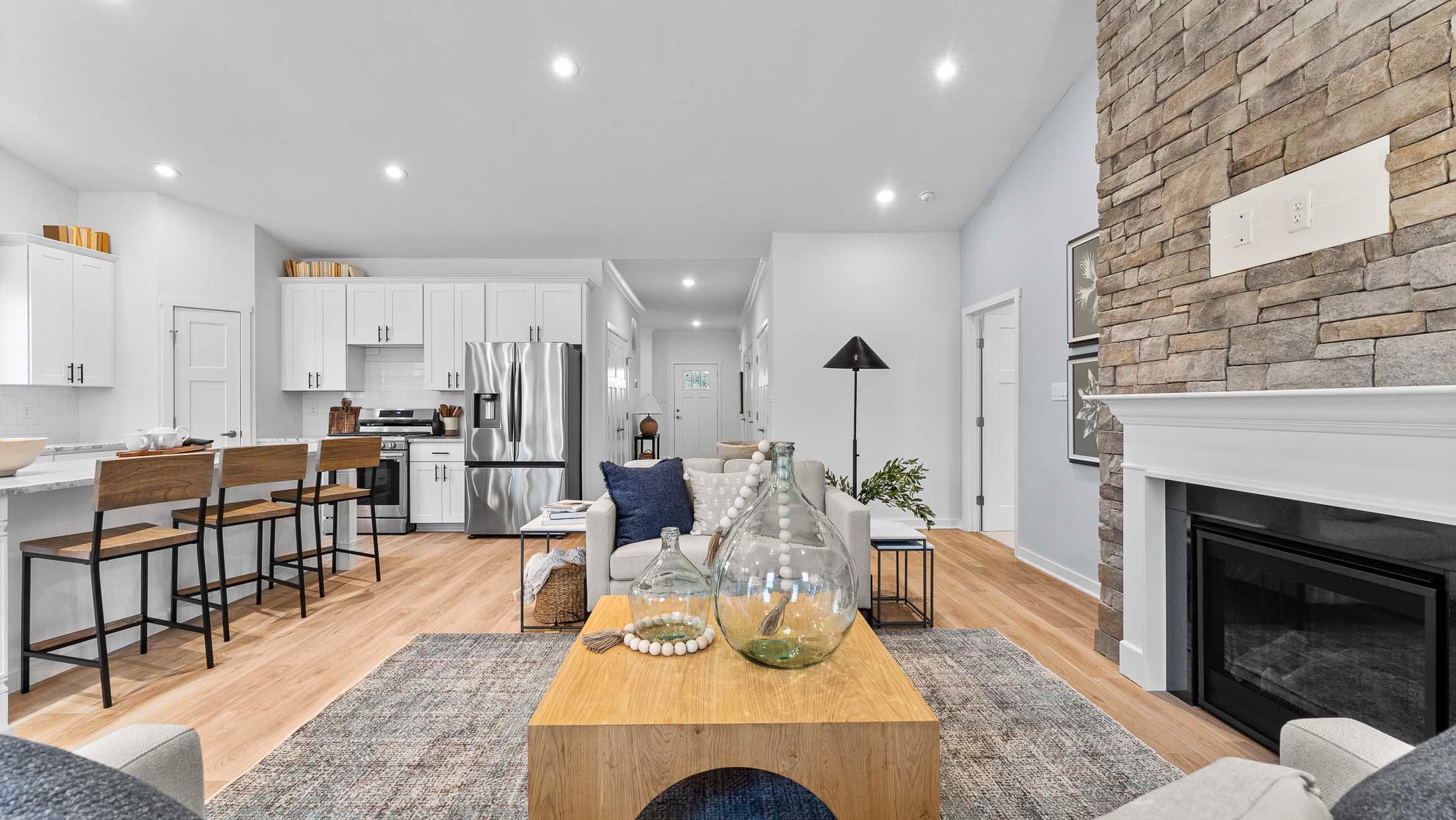 Modern open-concept living room and kitchen with stone fireplace and elegant decor.