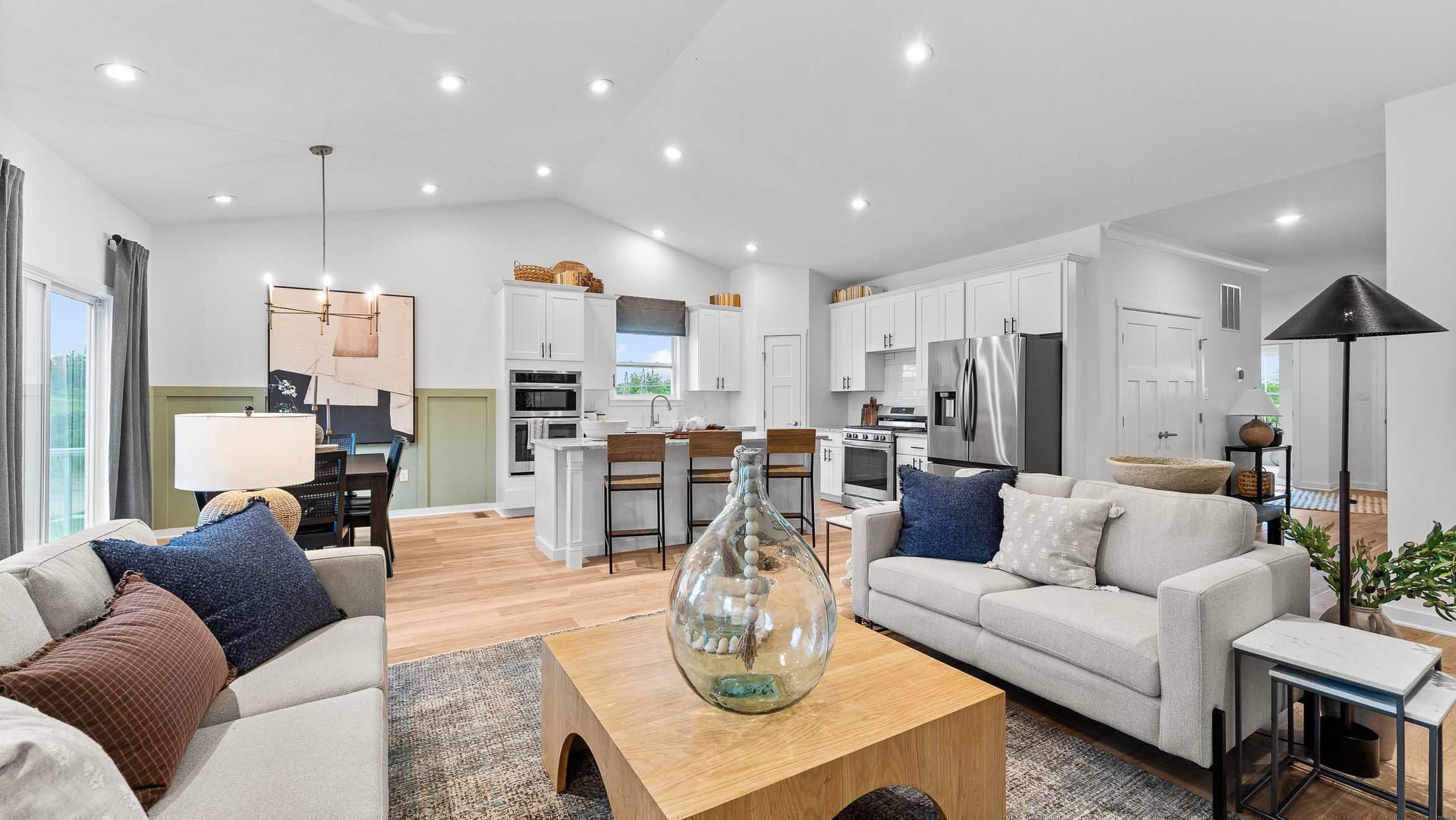 Modern open-concept living room and kitchen with white cabinets, stainless steel appliances, and stylish decor.