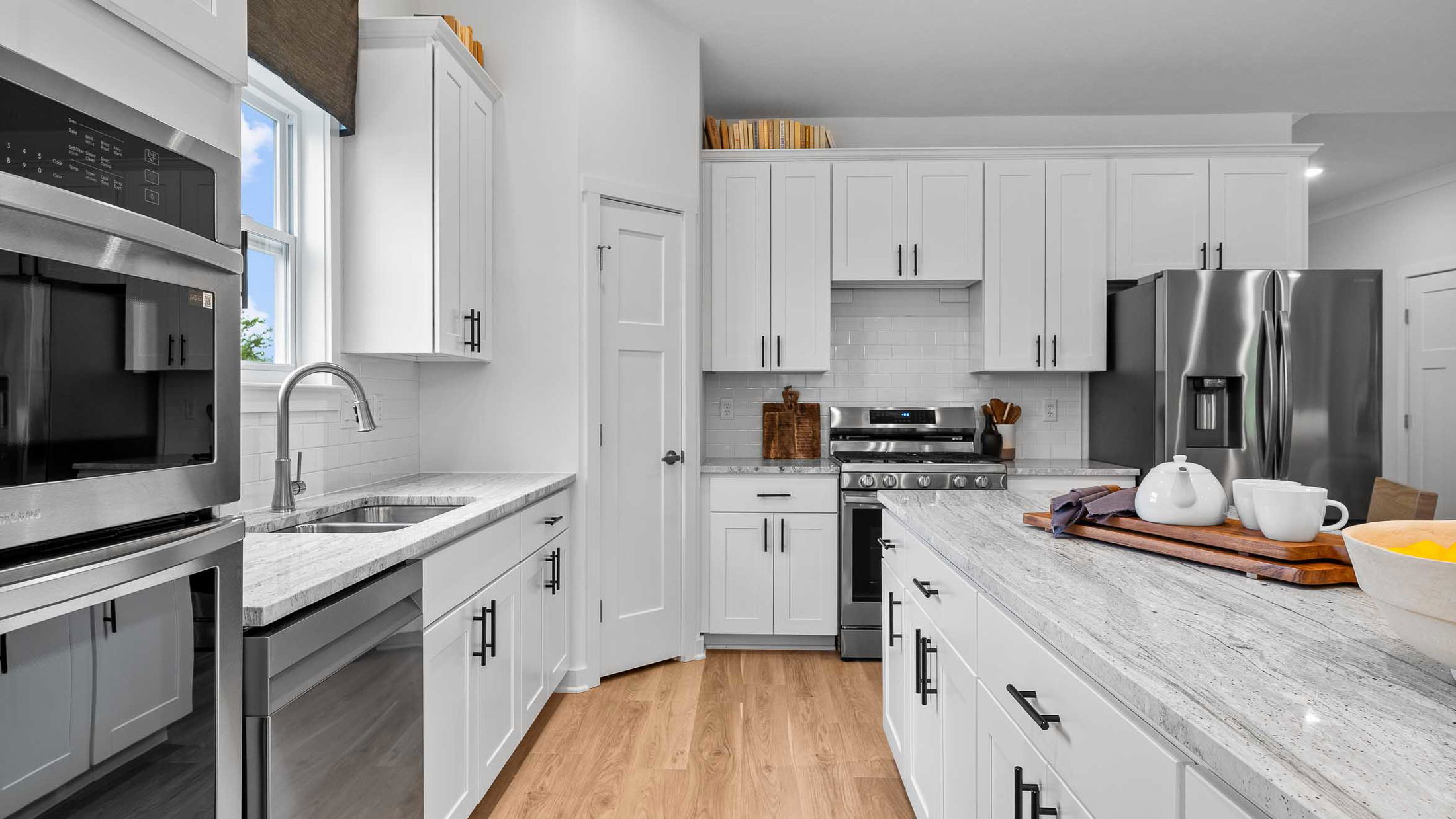 Modern kitchen with white cabinetry, stainless steel appliances, and a marble countertop island.