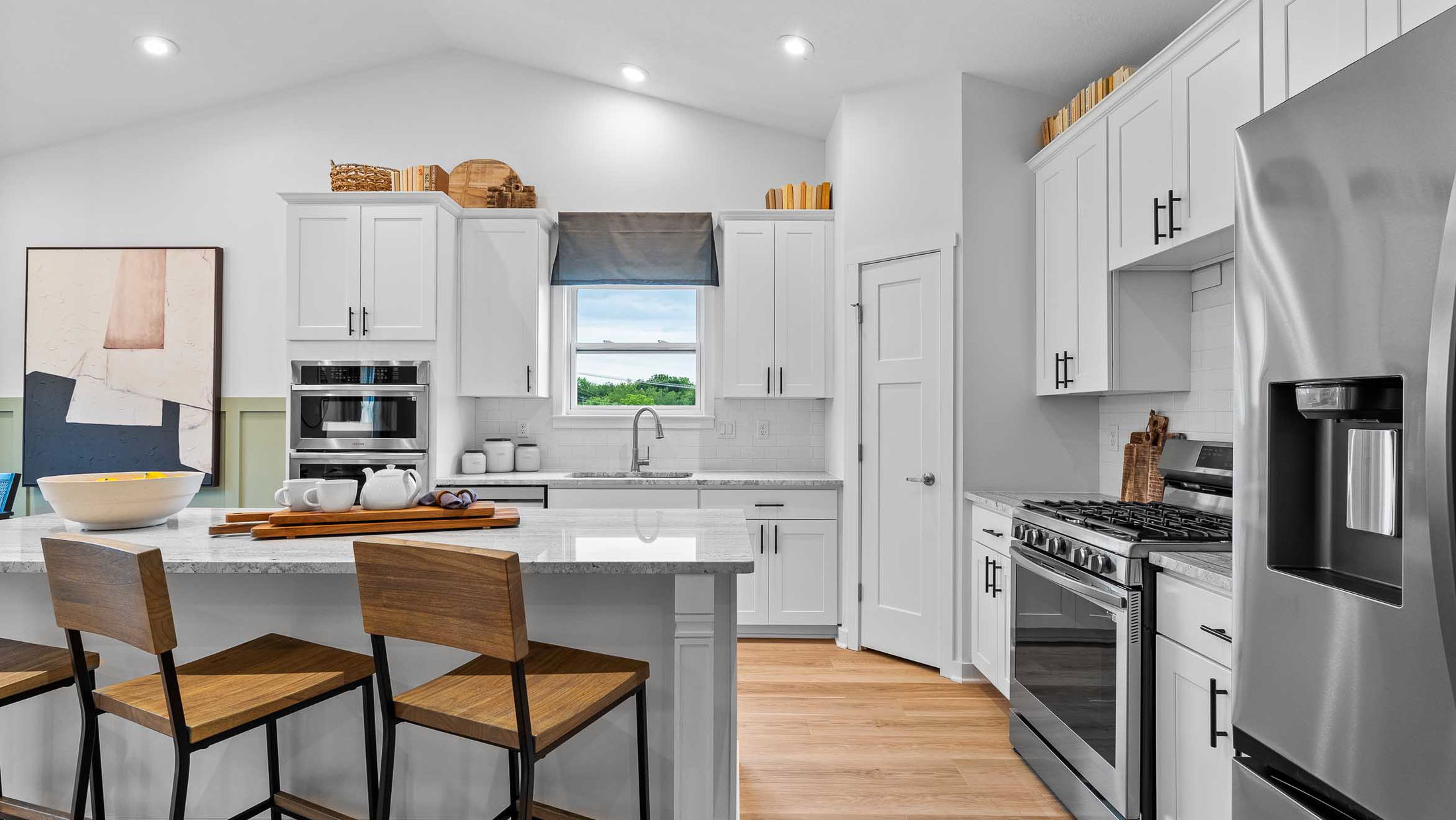 Modern kitchen interior with white cabinets, stainless steel appliances, and a central island with wooden chairs.