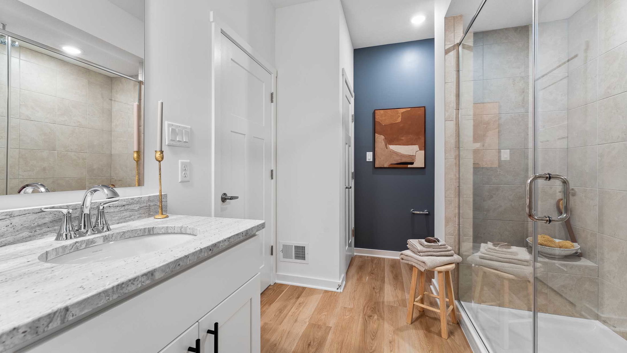 Modern bathroom featuring a glass-enclosed shower, wood flooring, and a stylish vanity with a granite countertop.
