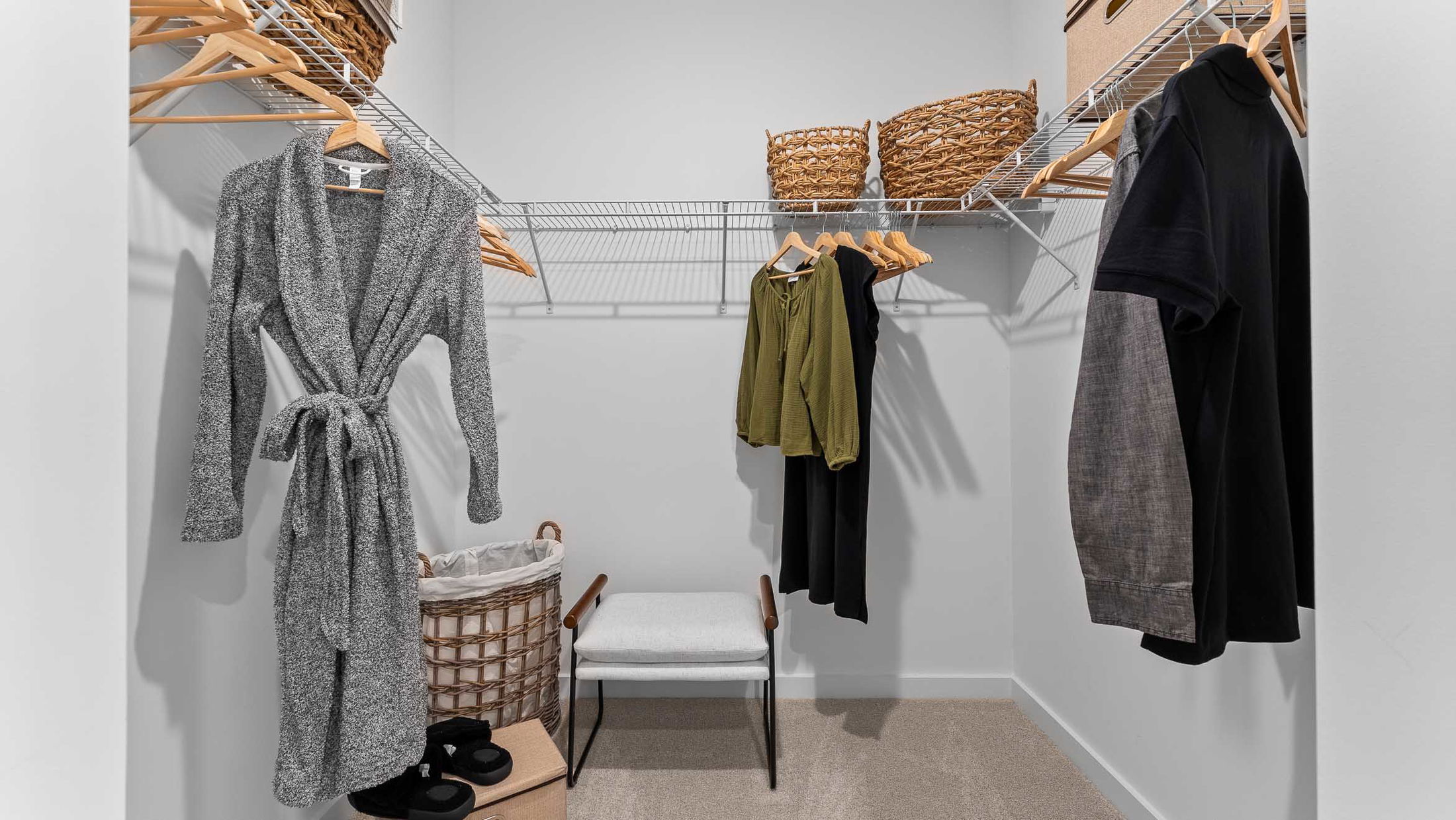 Walk-in closet with a robe, hanging clothes, wicker baskets, and a small bench.