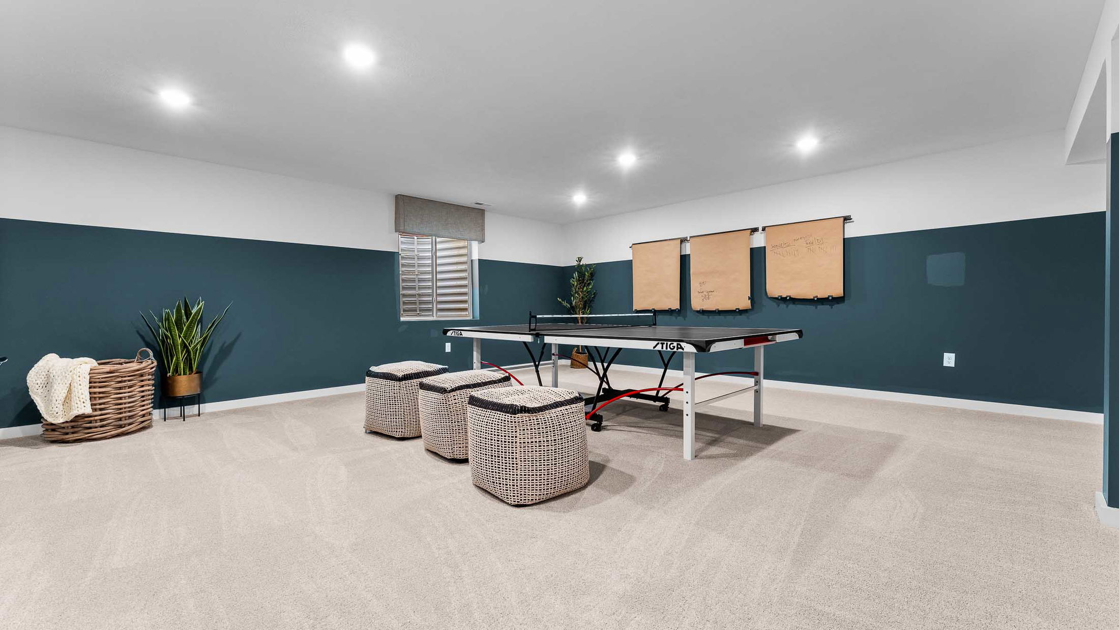 Stylish basement rec room featuring a ping pong table, wicker seating, and modern decor with a large basket and potted plant.