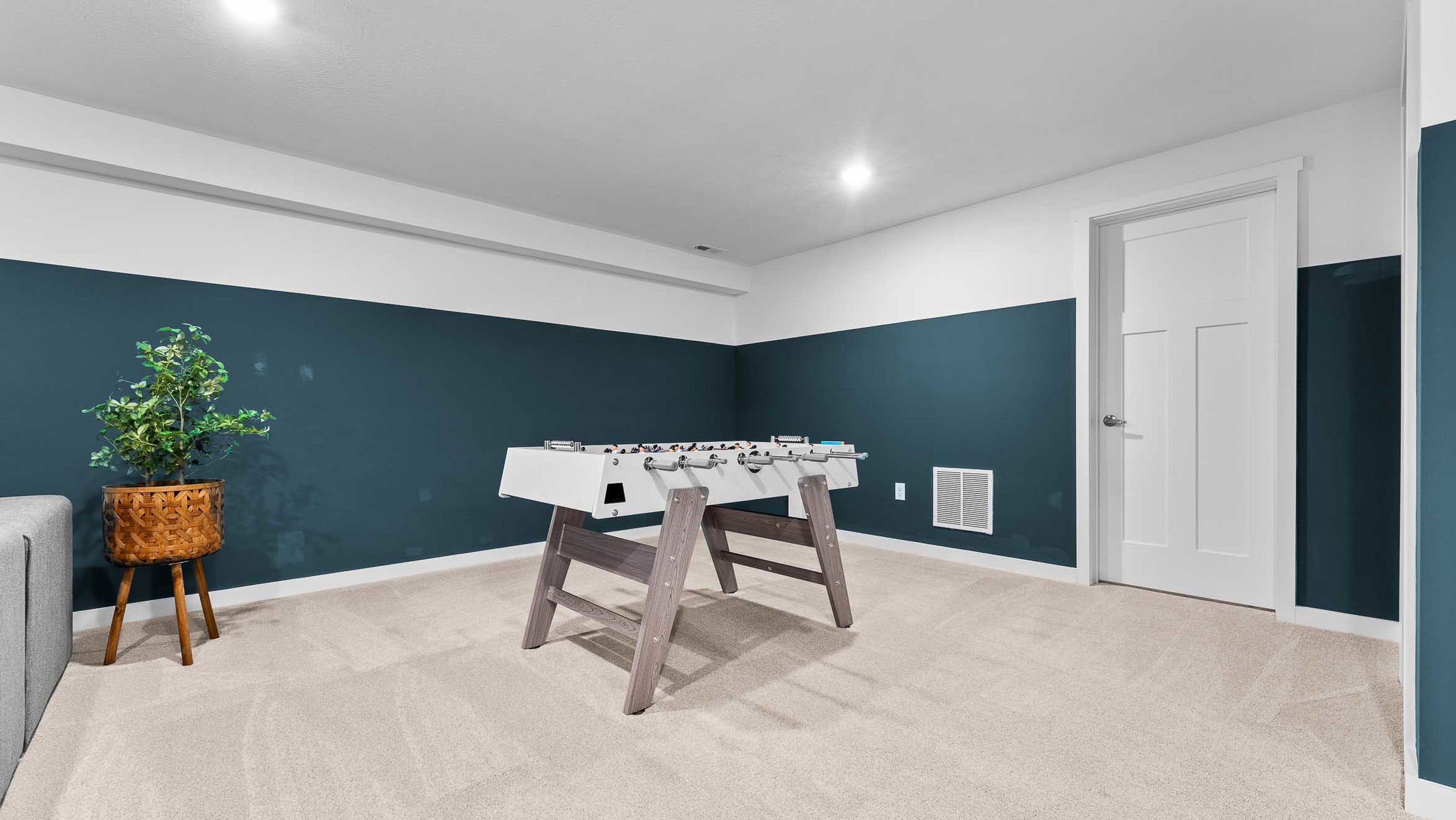Modern basement game room with a foosball table and potted plant on beige carpet.