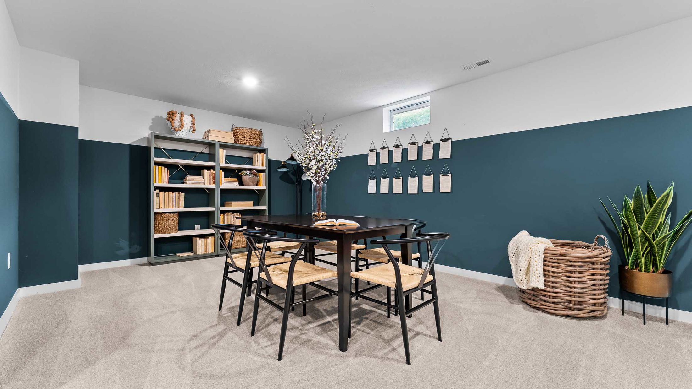 Modern home office with dark wood table, chairs, bookshelves, wall-mounted organizers, plant, and wicker basket with blanket.
