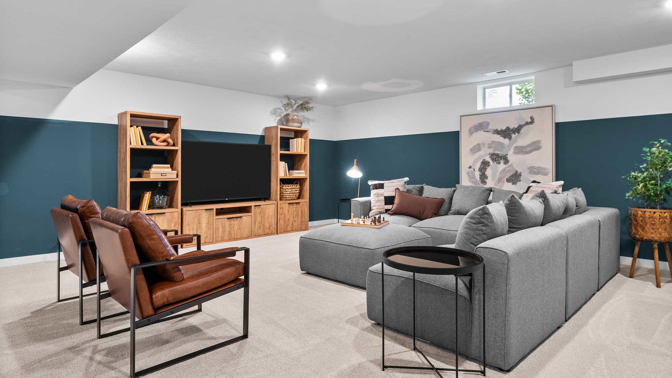 Modern living room with a large gray sectional sofa, wooden TV cabinet, and stylish decor, featuring teal accent walls and cozy seating.