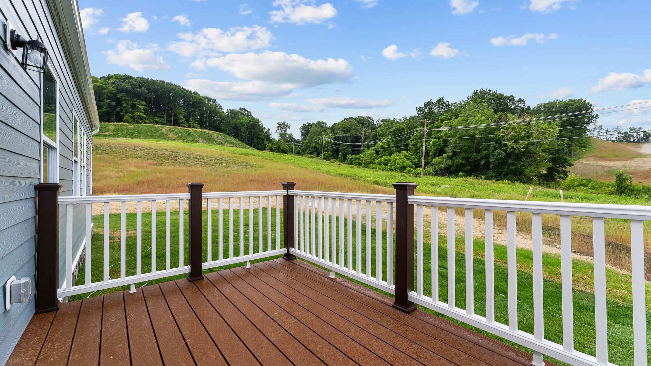 A spacious wooden deck with white railing overlooks a lush green landscape and clear blue sky.