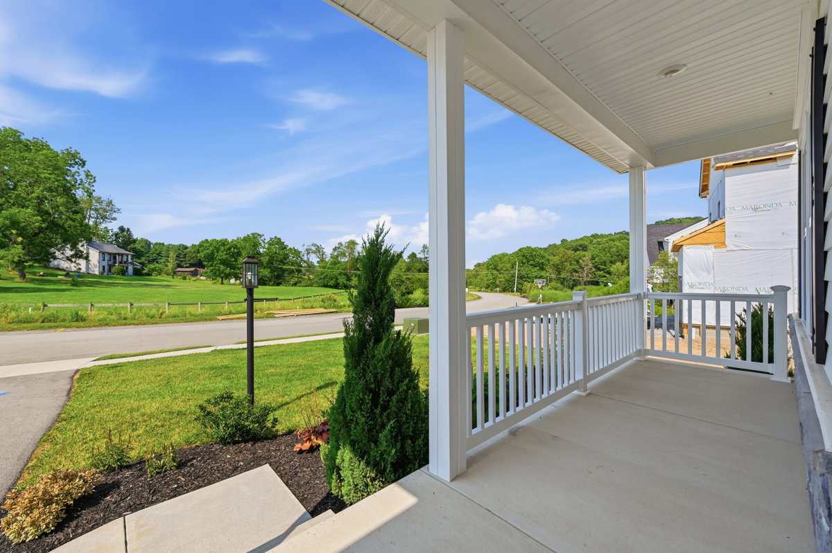 A front porch view showcasing greenery and a winding road on a sunny day.