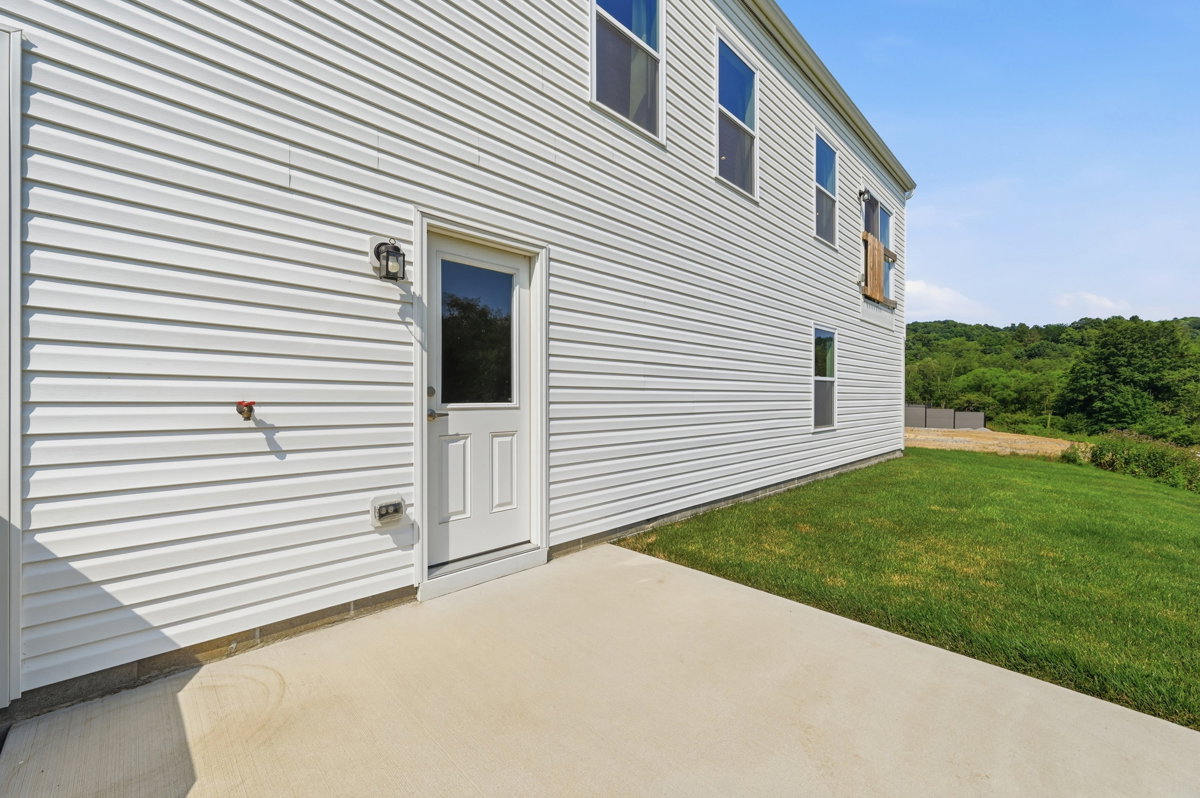 A white-clapboard exterior of a house with a door and a small lawn.