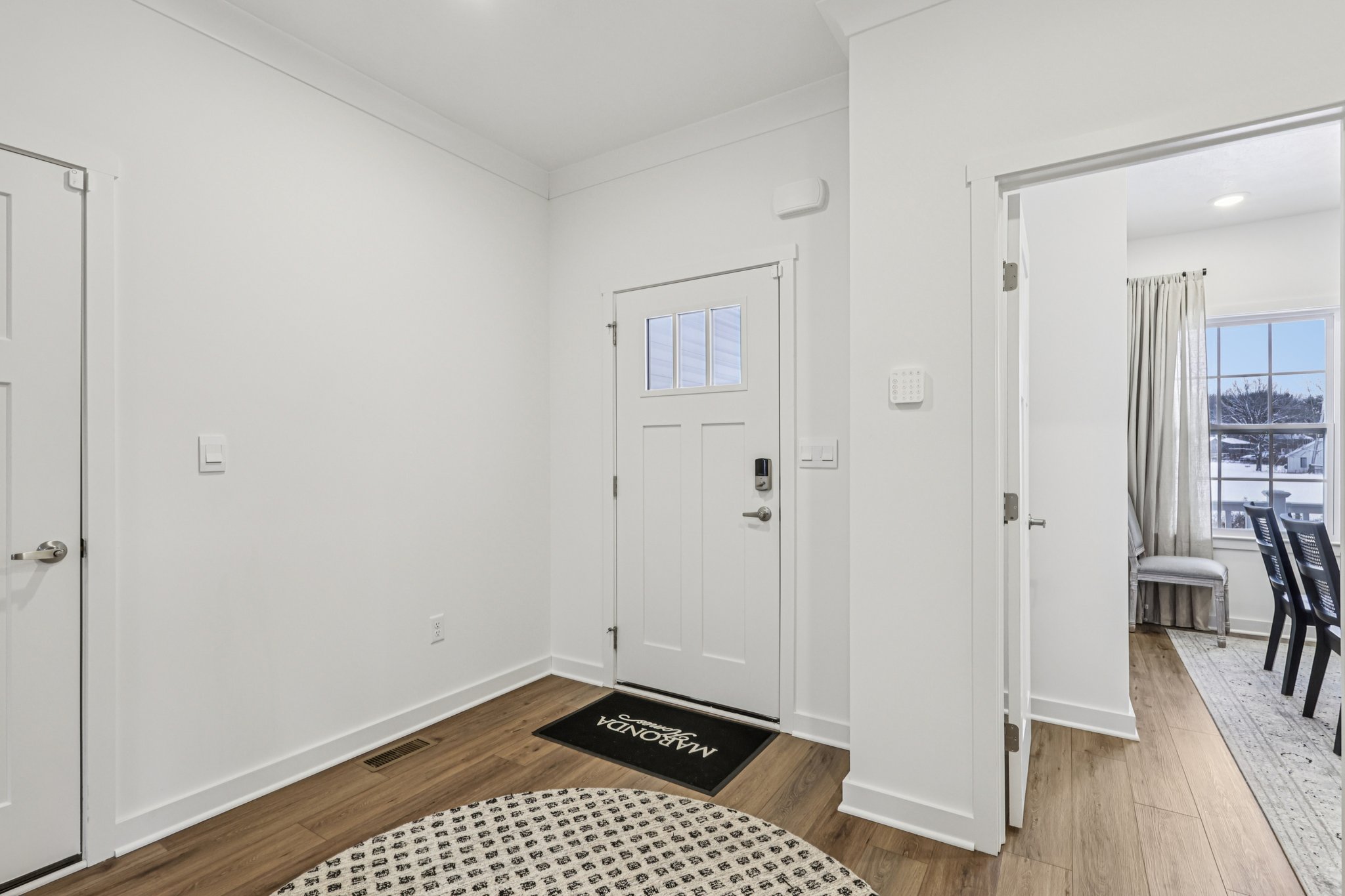 Bright entryway with a white door, round rug, and a view into a sitting area with large windows.