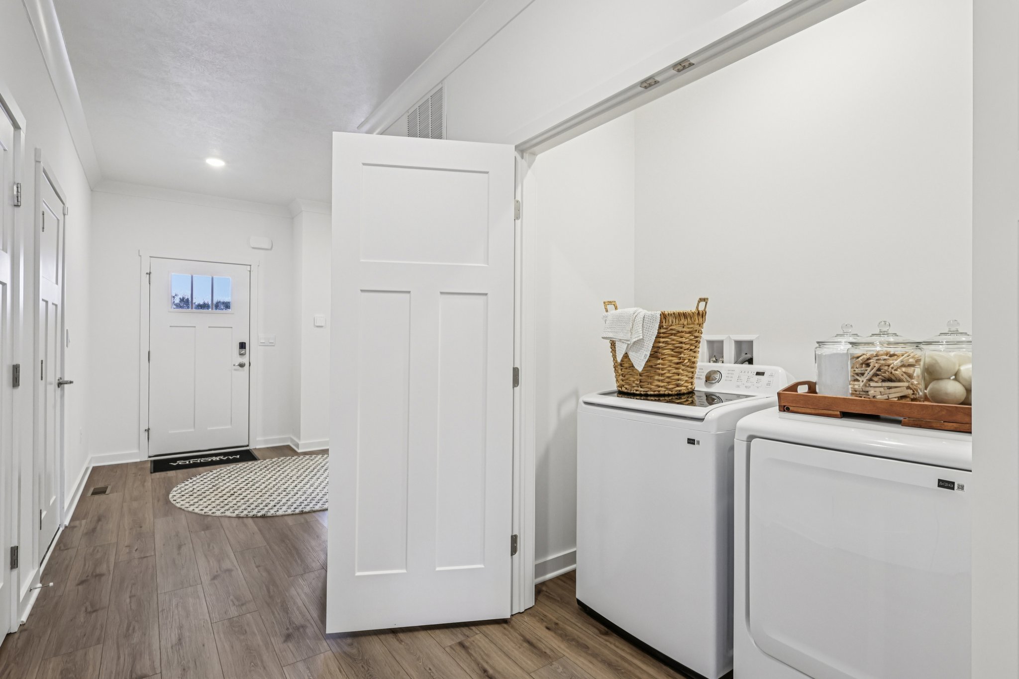 Bright laundry area with a white washer and dryer, wooden flooring, and a basket on a tray.