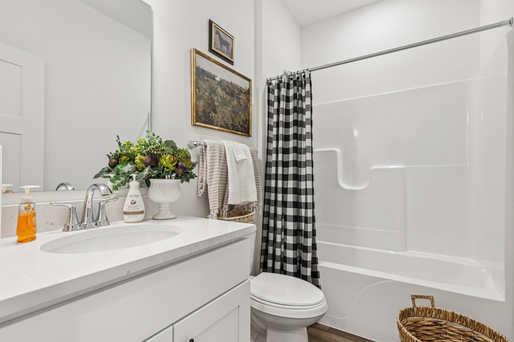 A modern bathroom featuring a white countertop, a shower/tub combination with a black and white checkered curtain, and decorative plants.