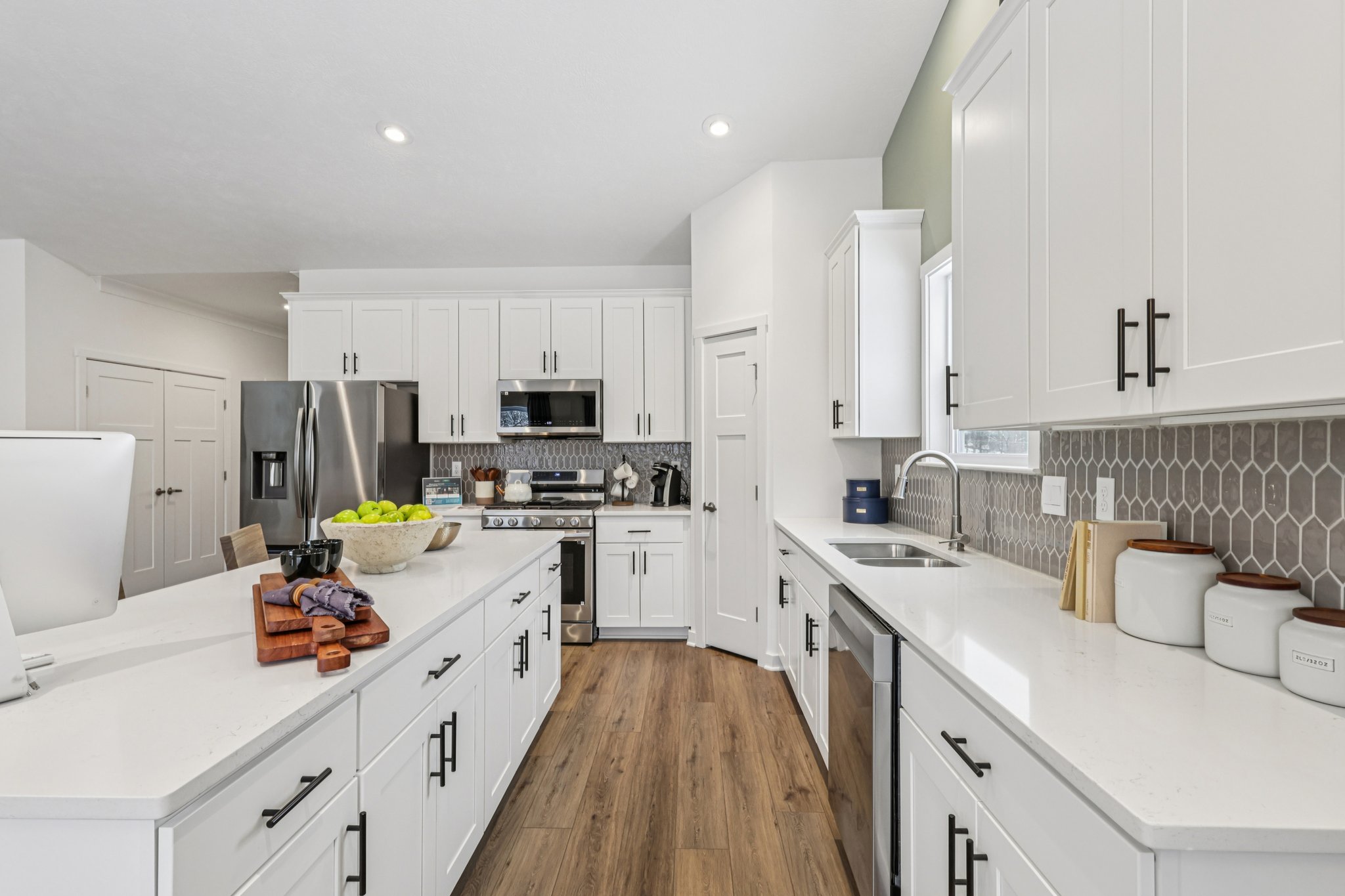 Modern kitchen with white cabinetry, stainless steel appliances, and a large island featuring a bowl of green apples.