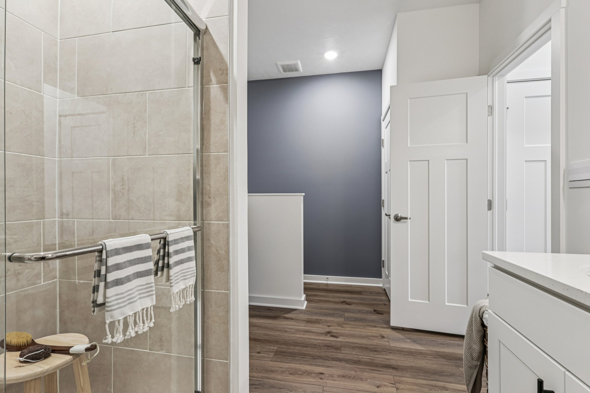 Modern bathroom interior featuring a glass shower, striped towels, and wooden flooring.