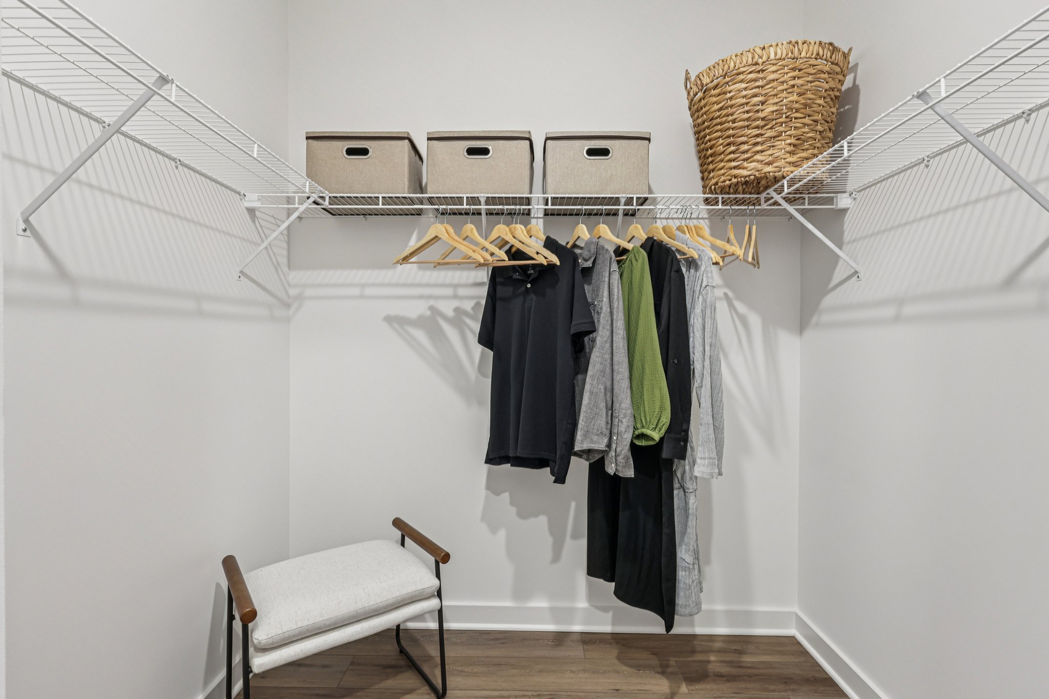 A closet featuring hanging clothes, storage boxes, a woven basket, and a small chair.