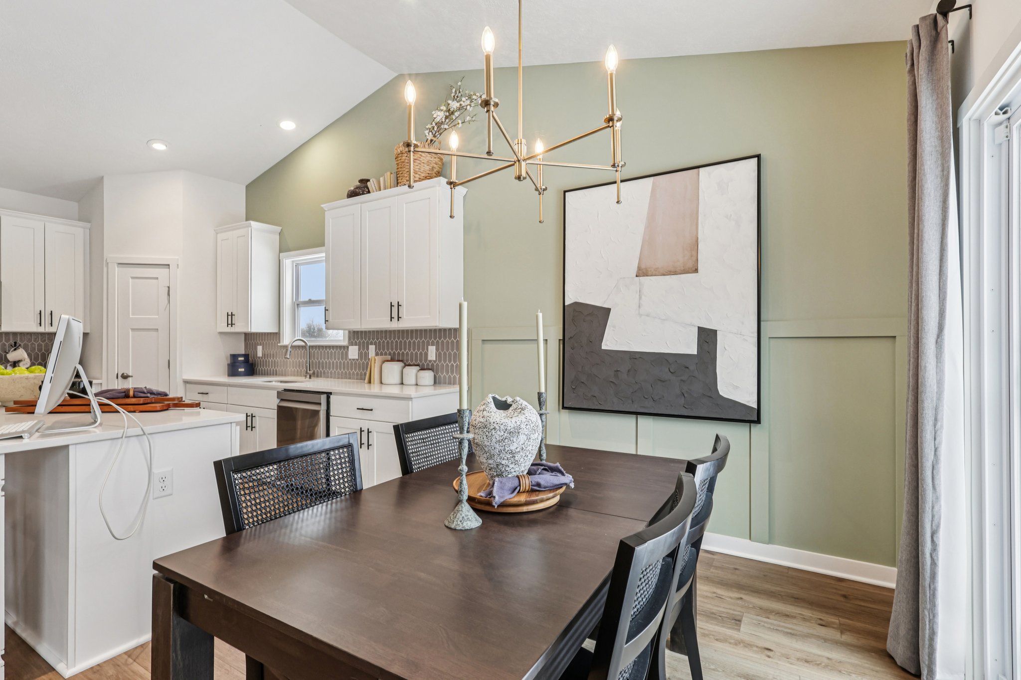 A modern kitchen and dining area featuring a wooden table, black chairs, and a light fixture, with a large abstract painting on the wall.