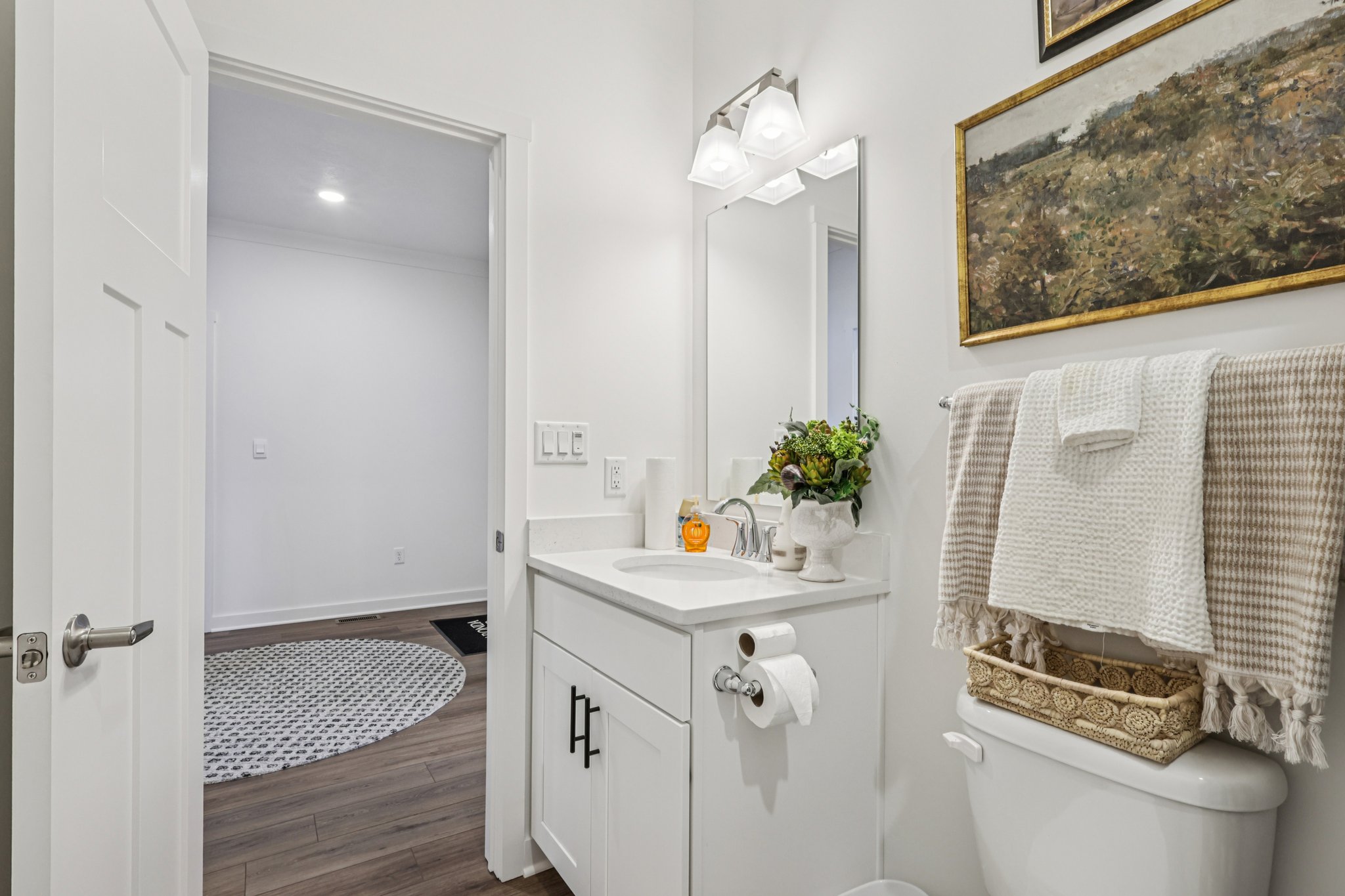 Bright bathroom with a white vanity, mirror, and decorative wall art, featuring a towel rack and potted plant.