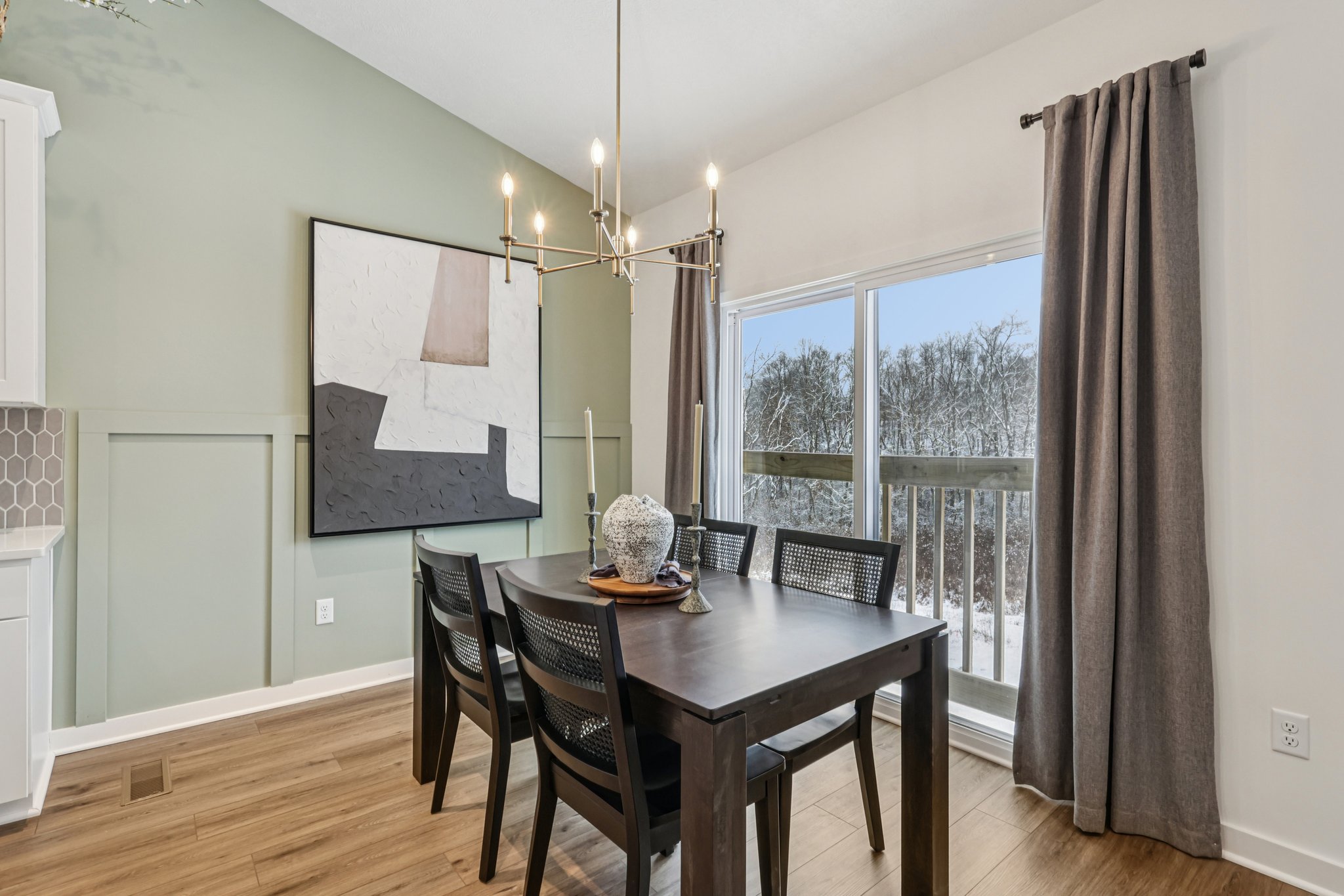 A modern dining room featuring a black table with six chairs, a wall art piece, and large windows with snowy outdoor views.