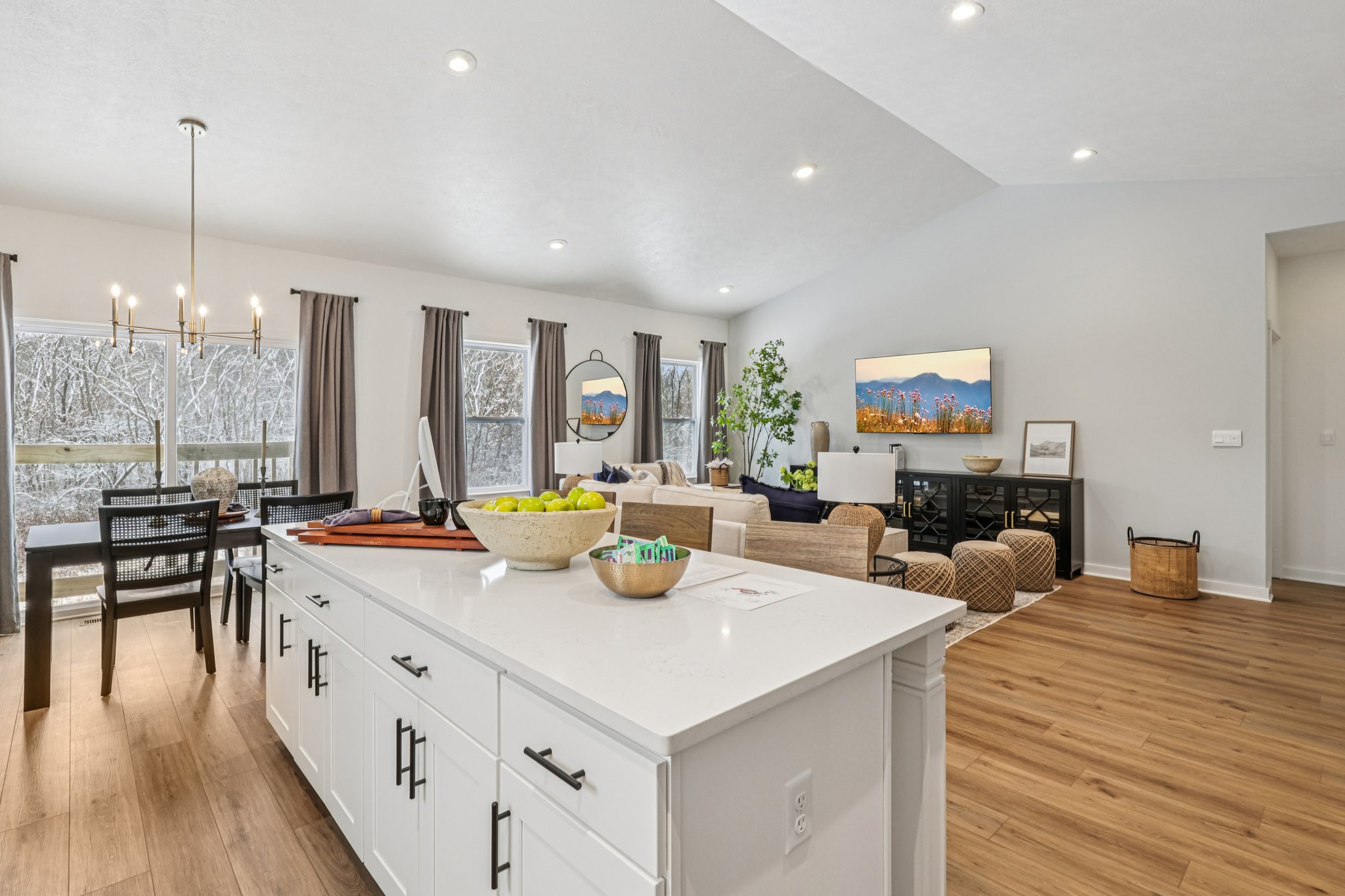 Contemporary living room and dining area featuring a large window, modern furniture, and a kitchen island with a bowl of fruit.