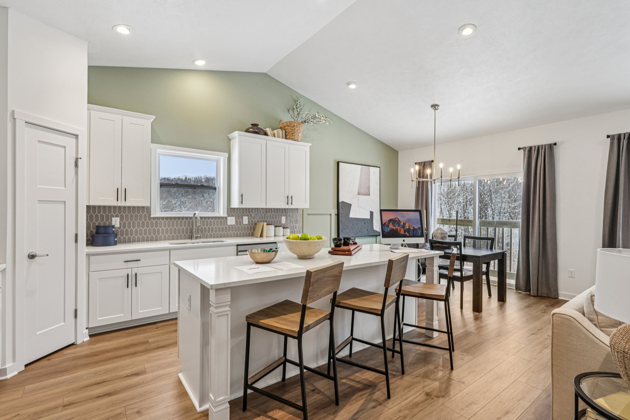 Modern kitchen featuring white cabinets, a large island with bar stools, and a dining area with a table and chairs.