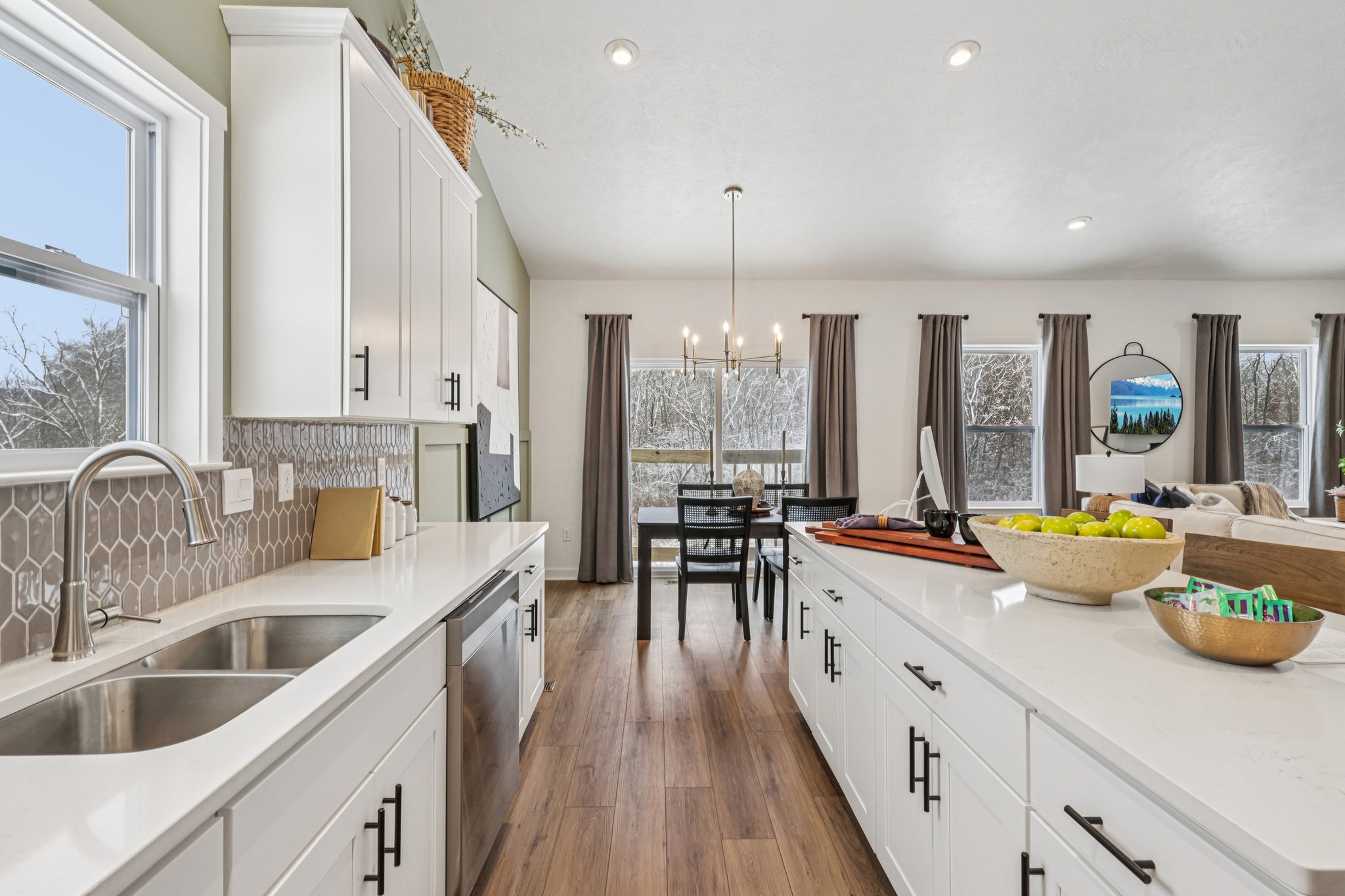 Bright kitchen featuring white cabinetry, a large sink, and a view of a dining area with natural light streaming in.