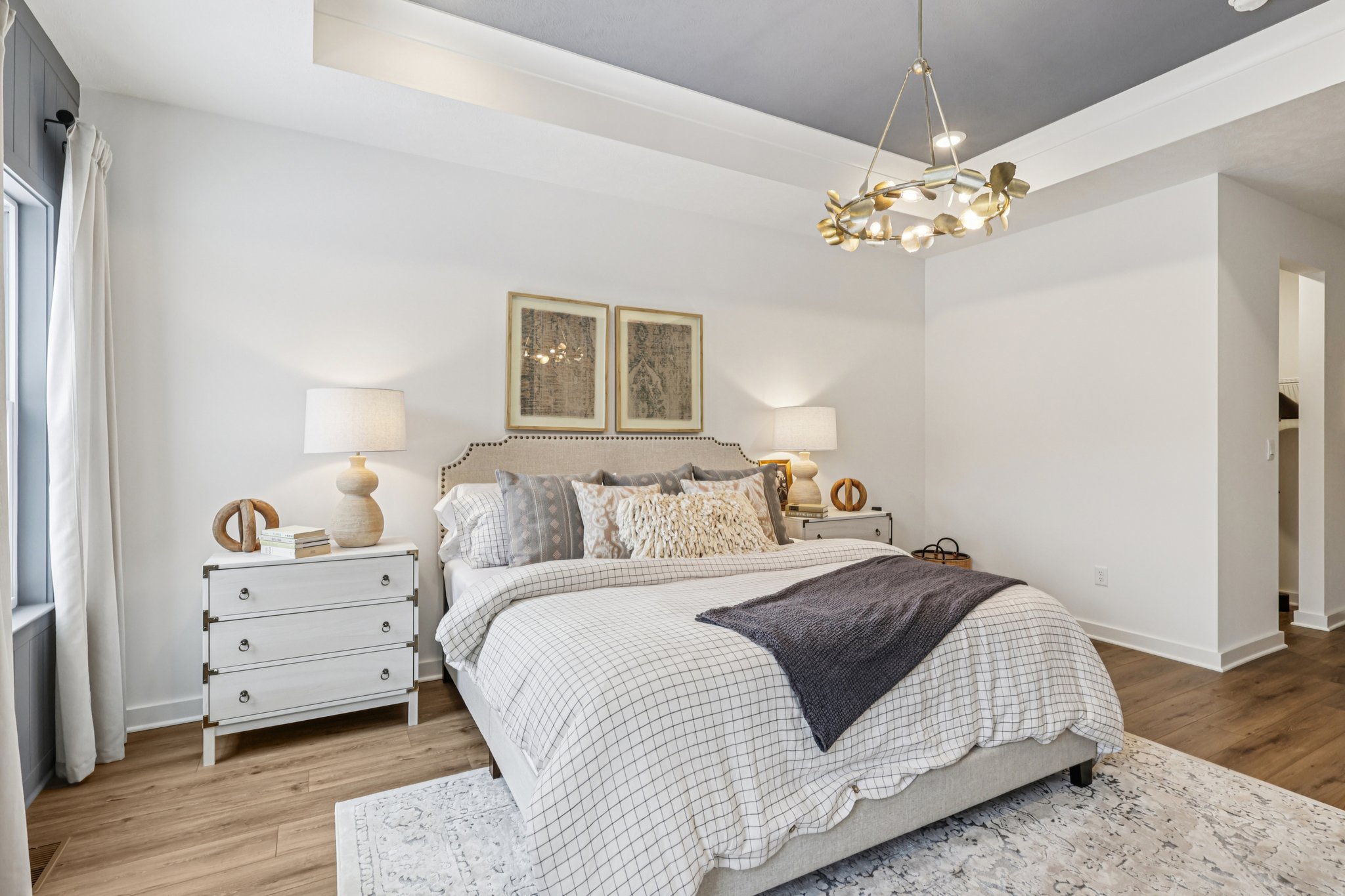 Bright and airy bedroom featuring a large bed with decorative pillows, two bedside lamps, and framed artwork on the wall.