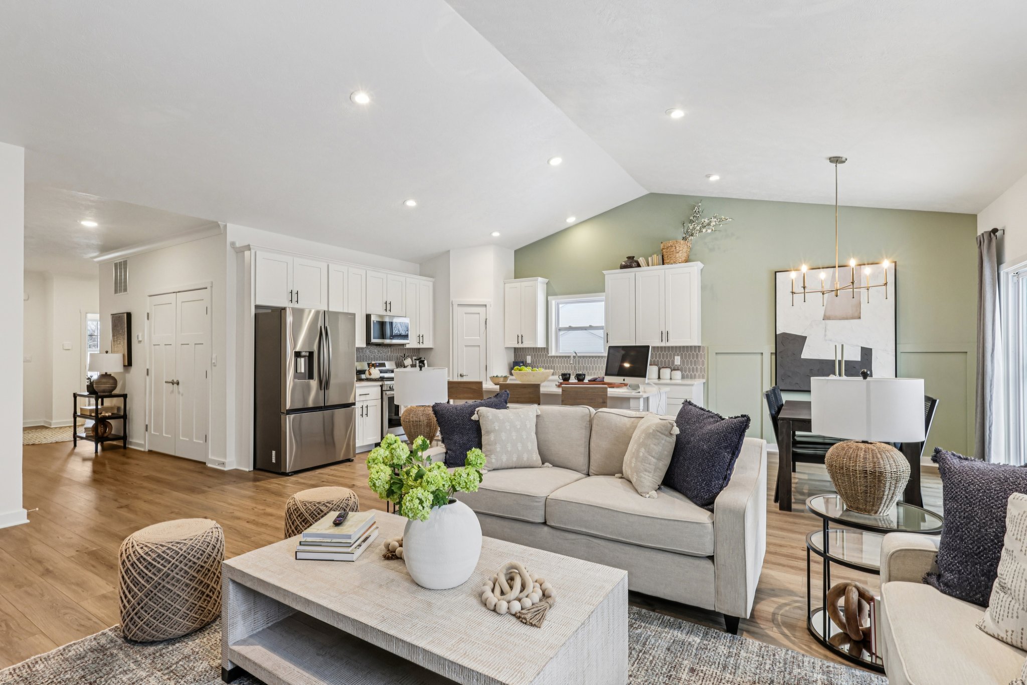 Bright, modern living area with a sectional sofa, coffee table, and open kitchen featuring stainless steel appliances.