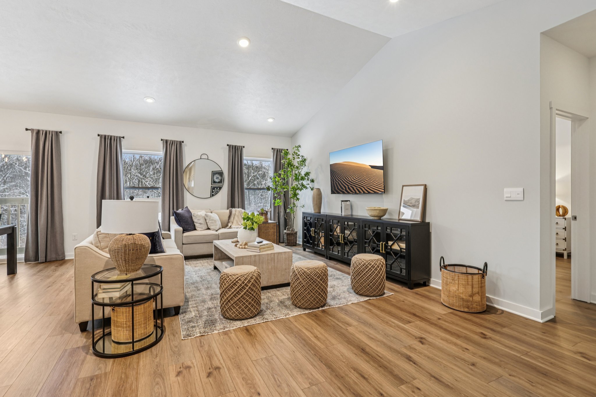 Bright modern living room with a sectional sofa, coffee table, decorative plants, and wall-mounted television.