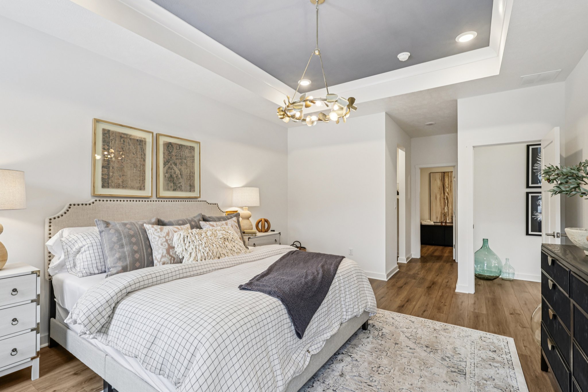 A modern bedroom featuring a neatly made bed with decorative pillows, a stylish chandelier, and framed artwork on the walls.