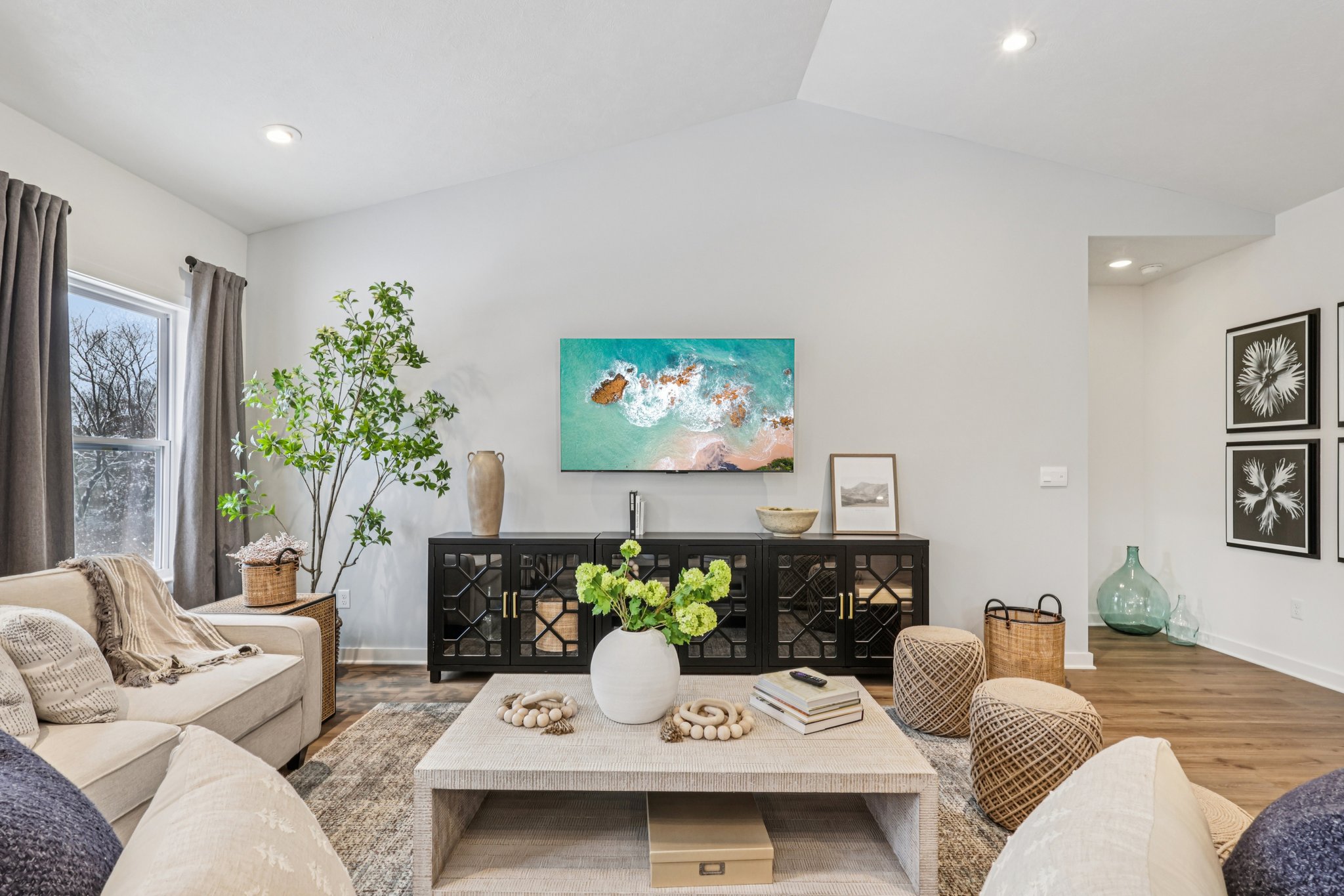 A modern living room featuring a light-colored sofa, a large television mounted on a wall, a coffee table with decorative items, and plants in a stylish setting.