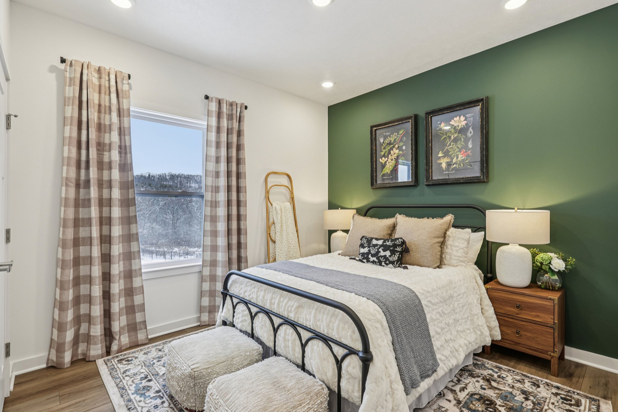A cozy bedroom featuring a dark green accent wall, a neatly made bed with decorative pillows, and two framed botanical prints.