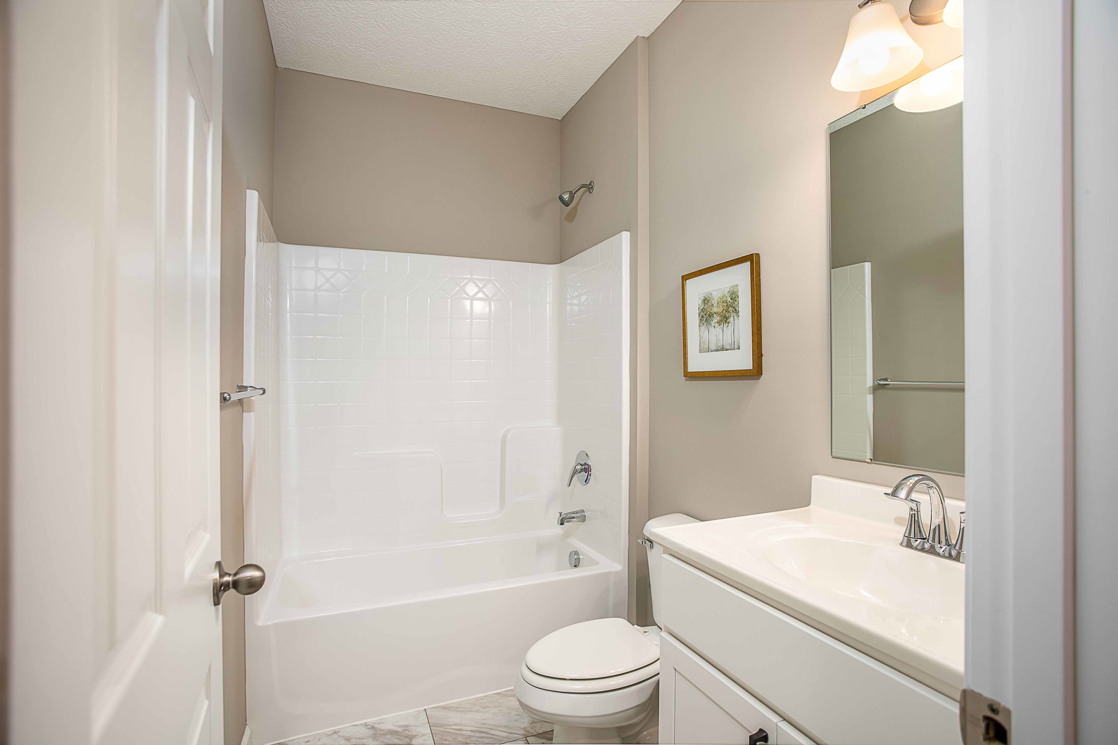 Modern bathroom with white bathtub, toilet, vanity, and framed artwork, featuring neutral-colored walls.