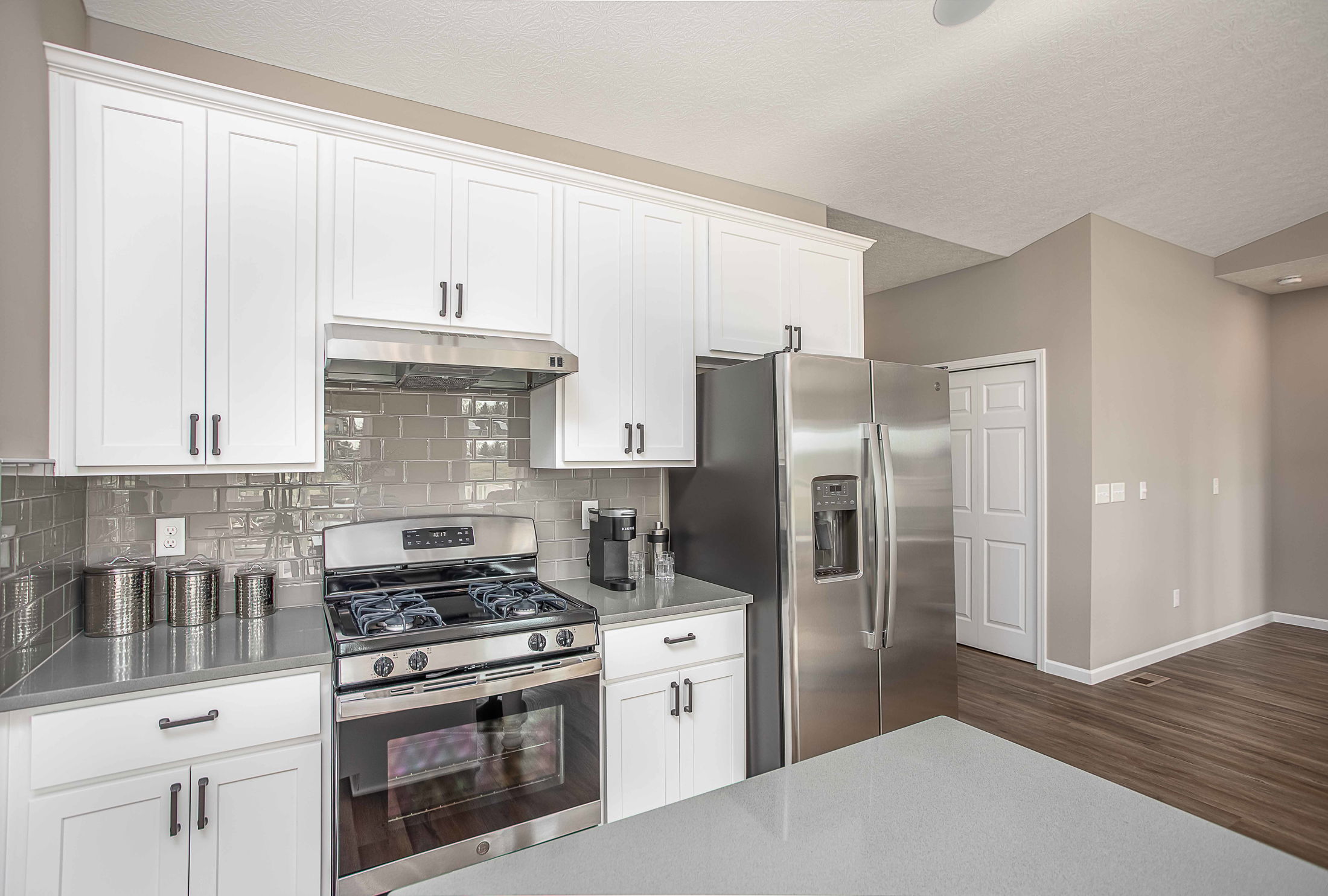 Modern kitchen with white cabinets, stainless steel appliances, and gray tile backsplash.