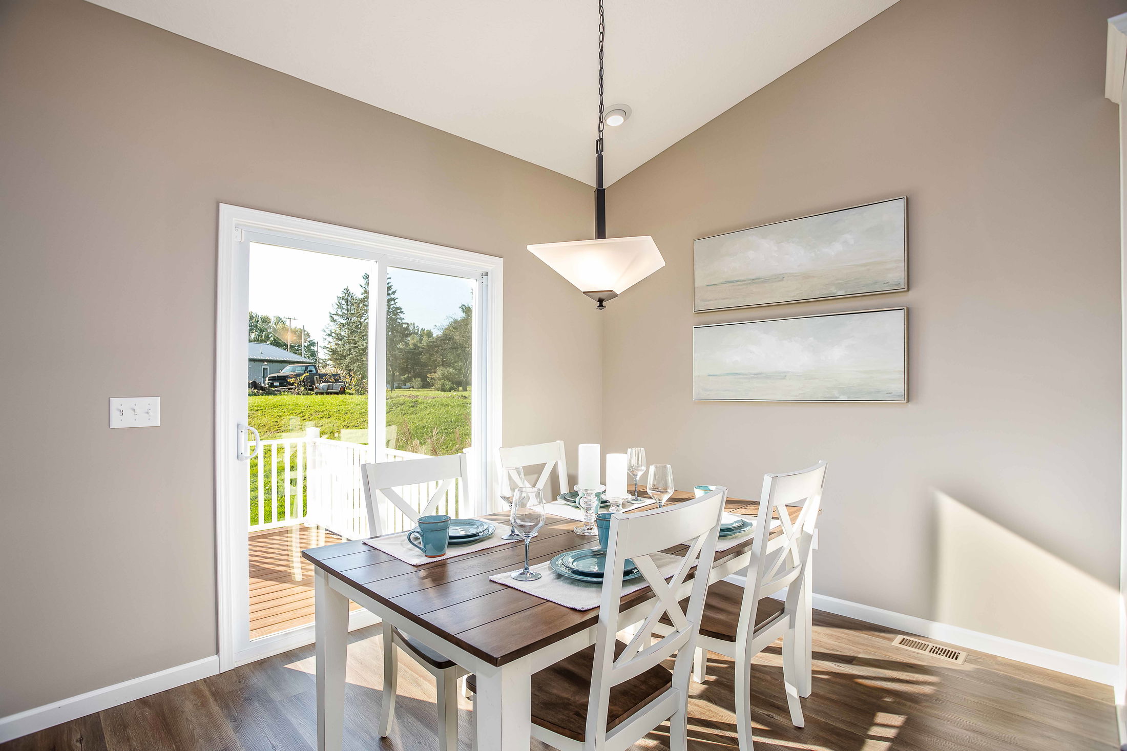 Modern dining room with a wooden table, white chairs, and a view of the backyard through sliding glass doors.