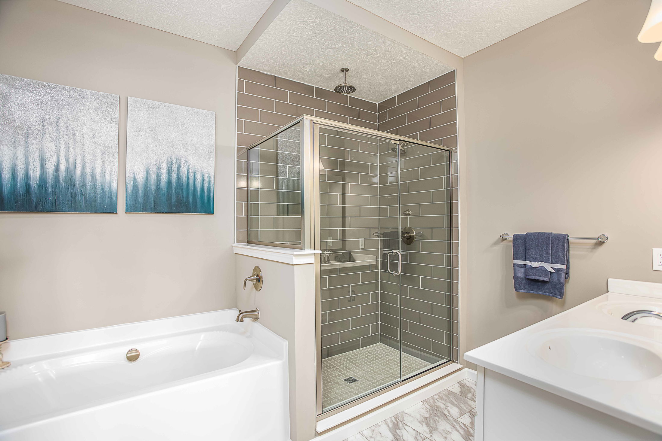 Modern bathroom interior with a glass shower enclosure, bathtub, abstract wall art, and a towel rack.
