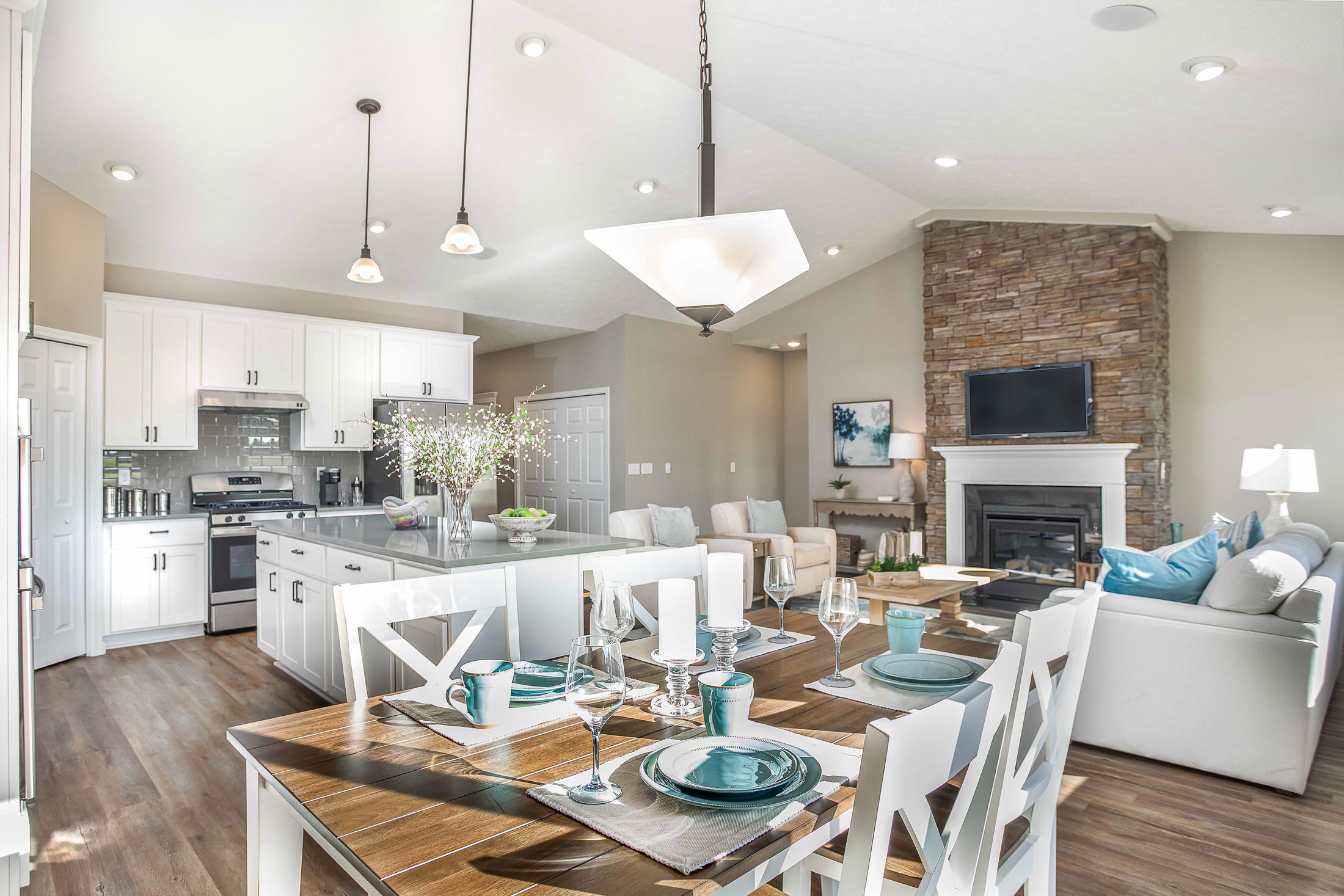 Modern open-concept kitchen and living room with white cabinetry, a stone fireplace, and elegant dining table setup.