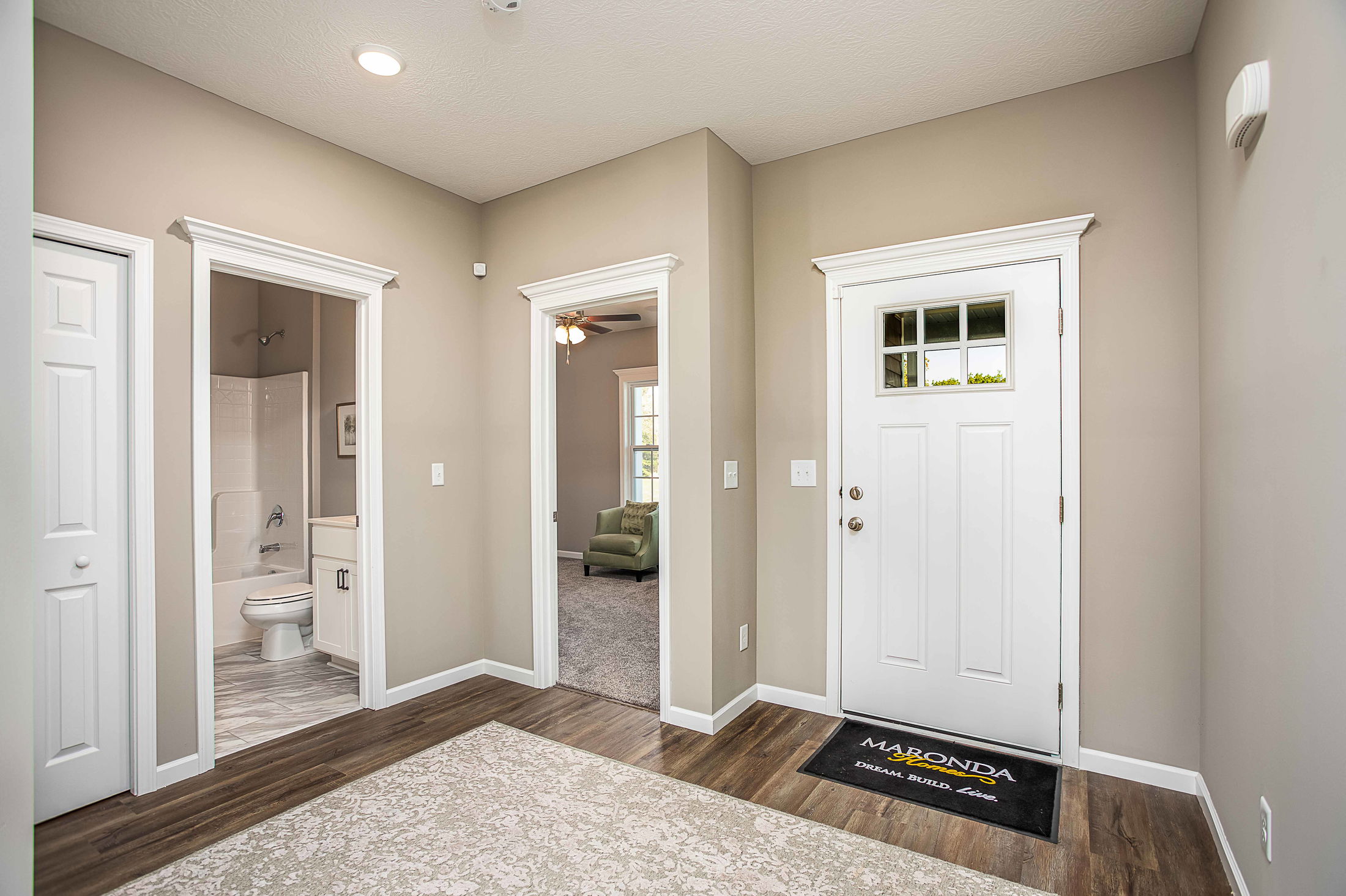 Modern entryway with white doors, wood flooring, and a glimpse into a bathroom and living room.