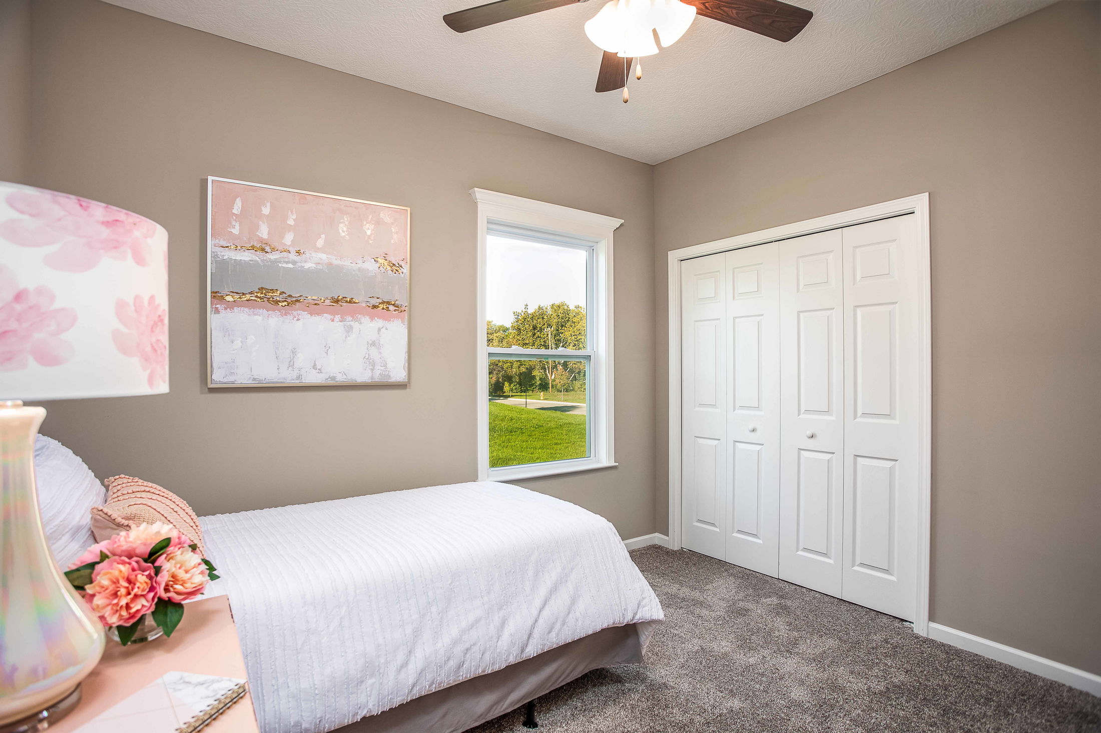 Cozy bedroom with beige walls, a single bed dressed in white linens, elegant wall art, and a scenic view window.