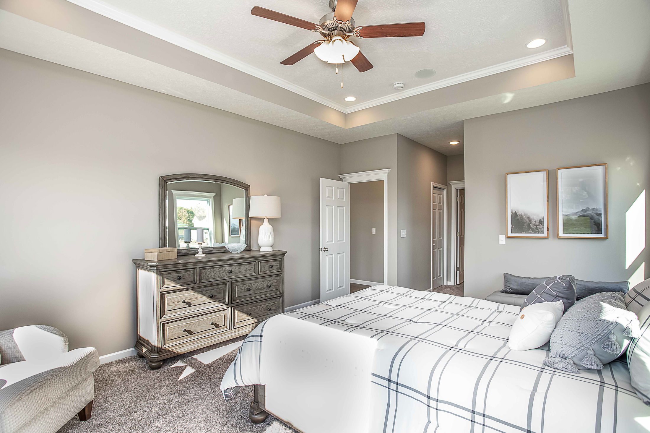 Modern bedroom interior featuring a comfortable bed with plaid bedding, a stylish gray accent wall, ceiling fan, and a wooden dresser with a mirror.