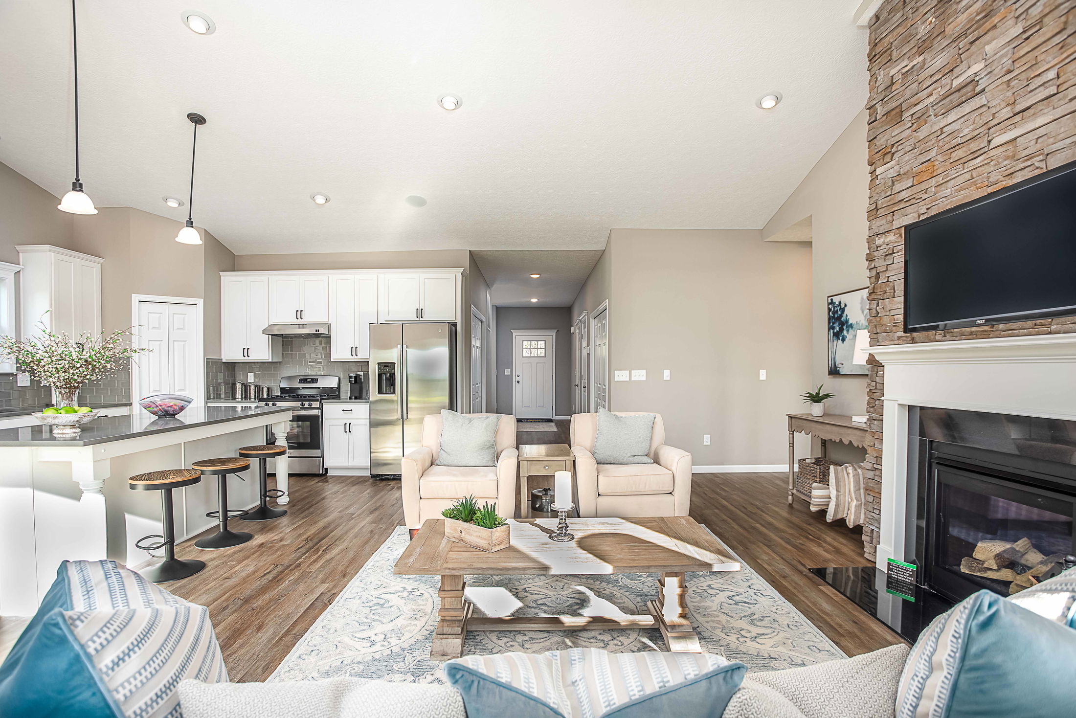 Modern open-concept living room and kitchen with white cabinetry, stone fireplace, and hardwood floors.