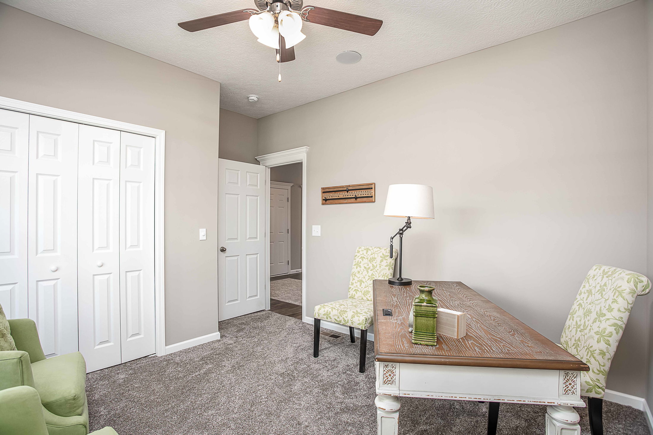 Bright, minimalist home office with a wooden desk, floral chairs, and a ceiling fan.