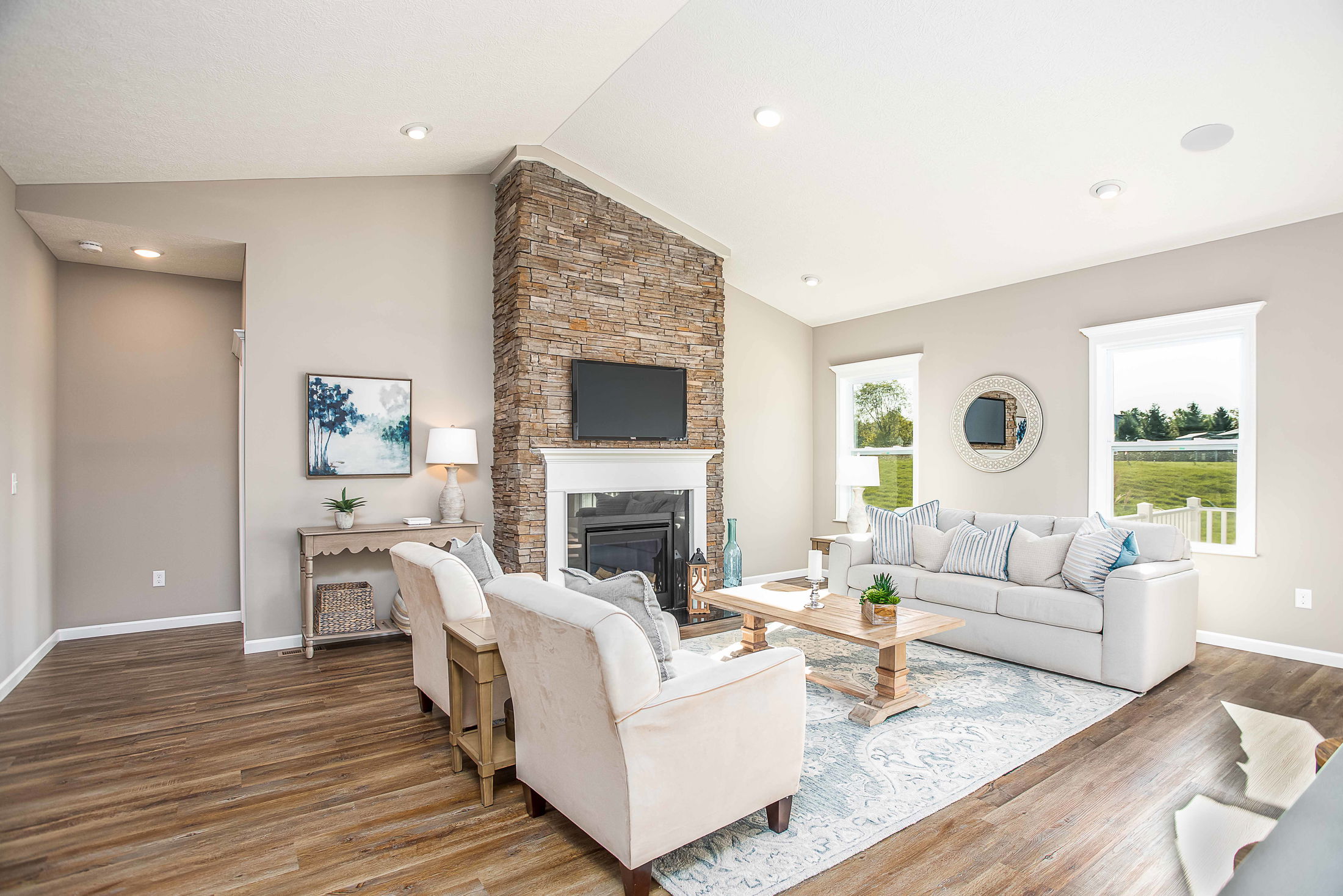 Elegant modern living room with a stone fireplace, hardwood floors, beige furniture, and large windows.