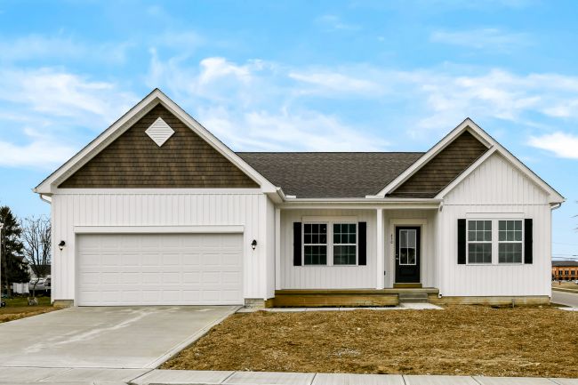 Modern suburban single-story white house with a two-car garage and gabled roof against a blue sky.