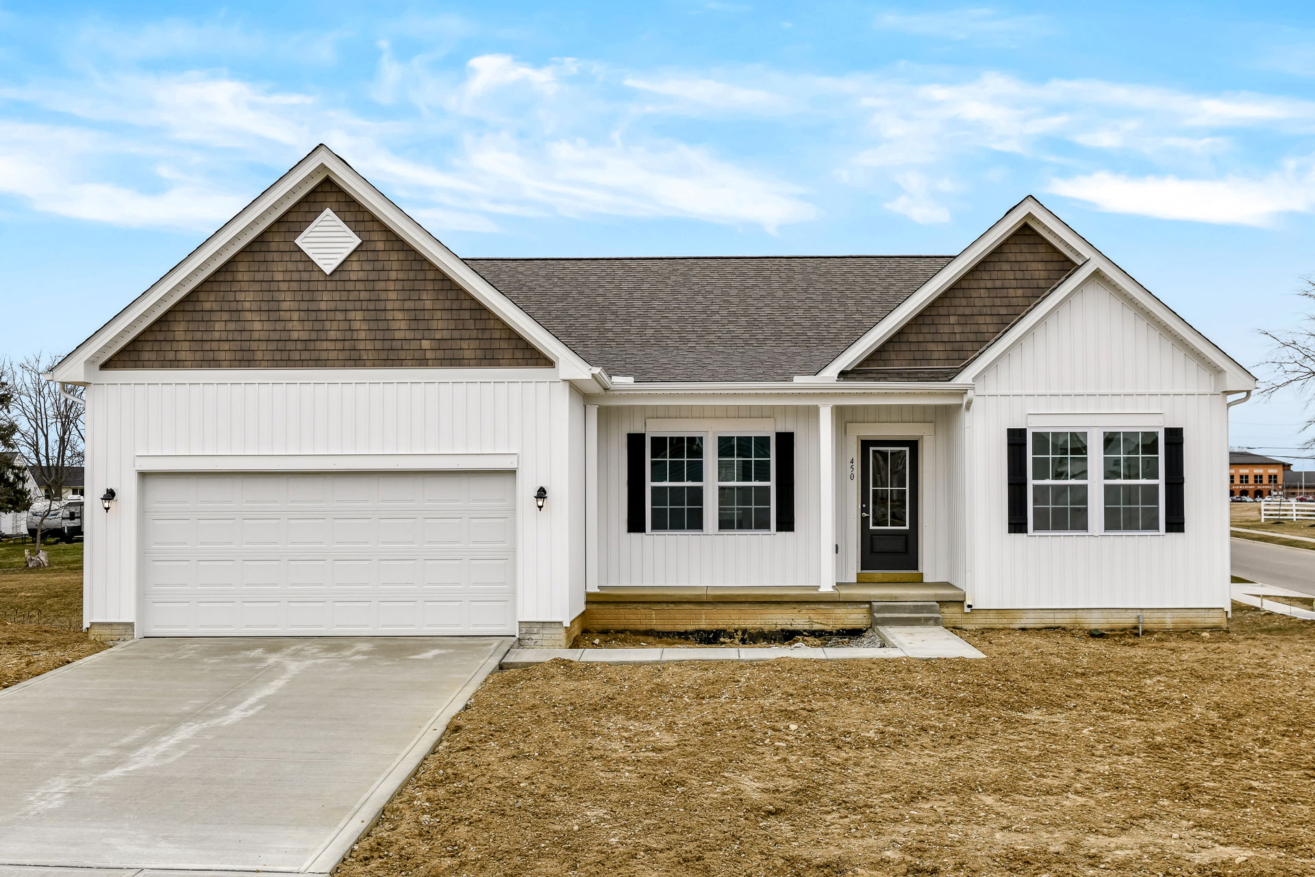A modern, newly built white ranch-style house with a double garage and black shutters under a clear blue sky.