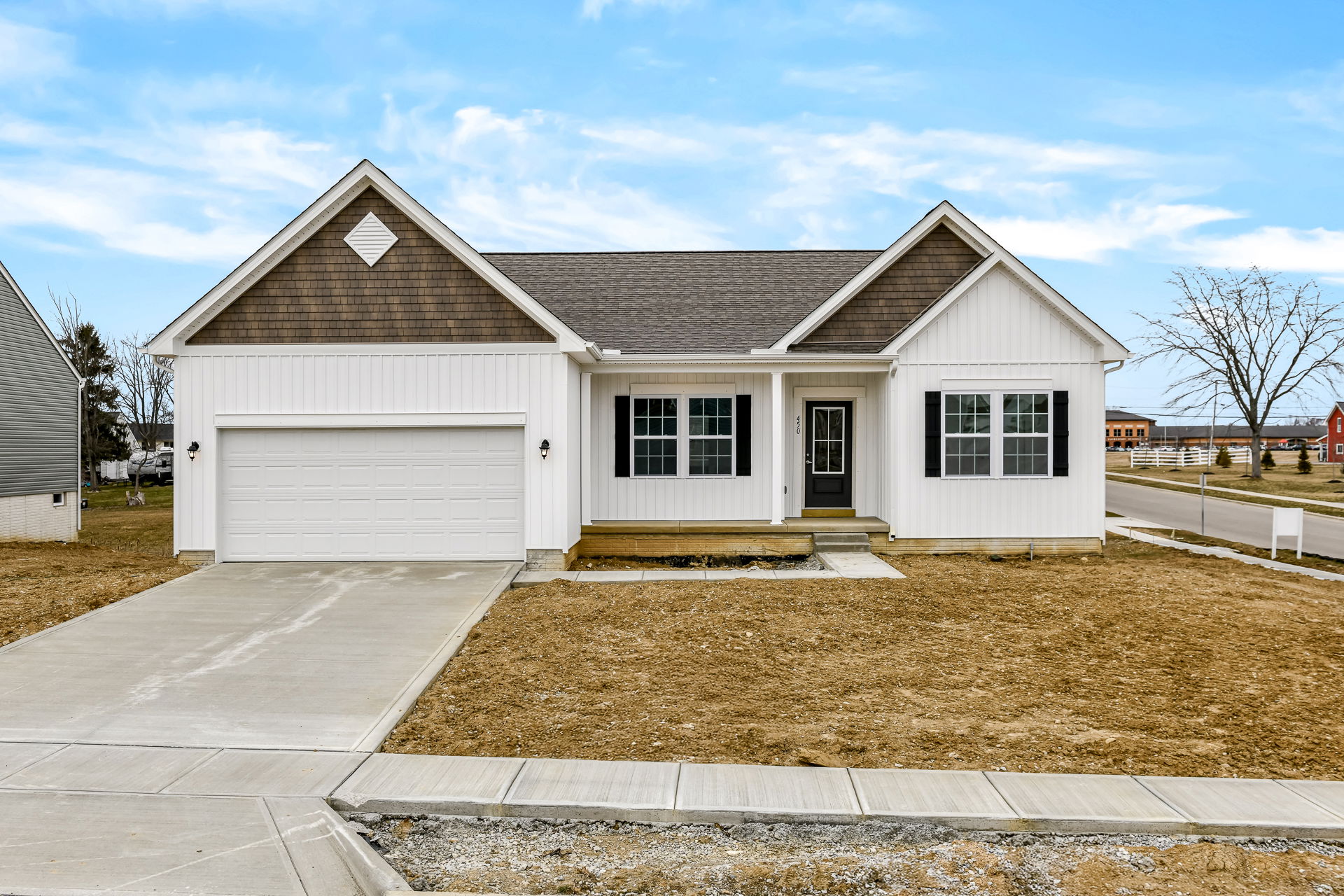 Newly constructed white suburban home with a gable roof, attached garage, and unfinished landscaping.