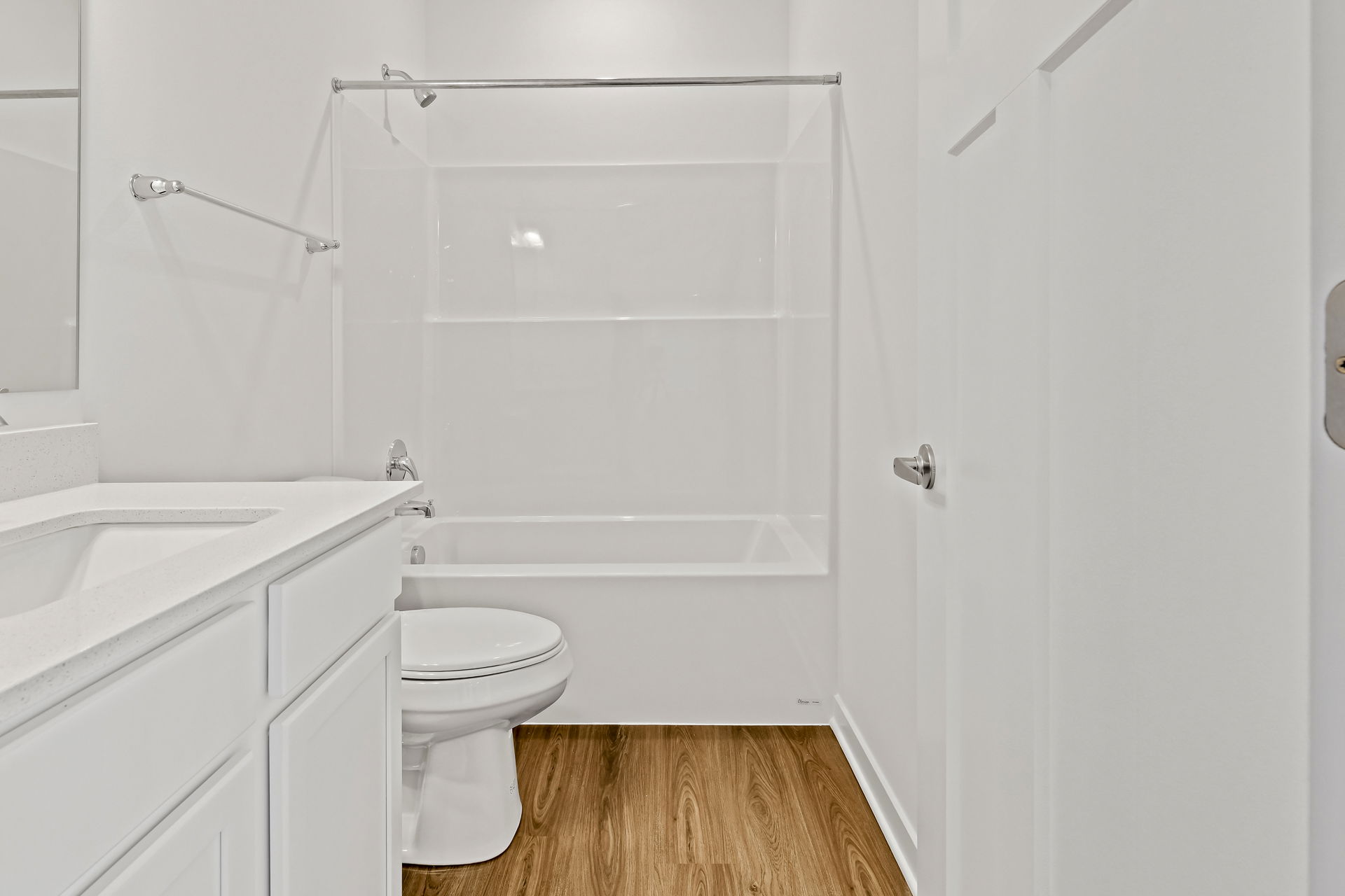Modern white bathroom with wood flooring, featuring a bathtub, toilet, and vanity.