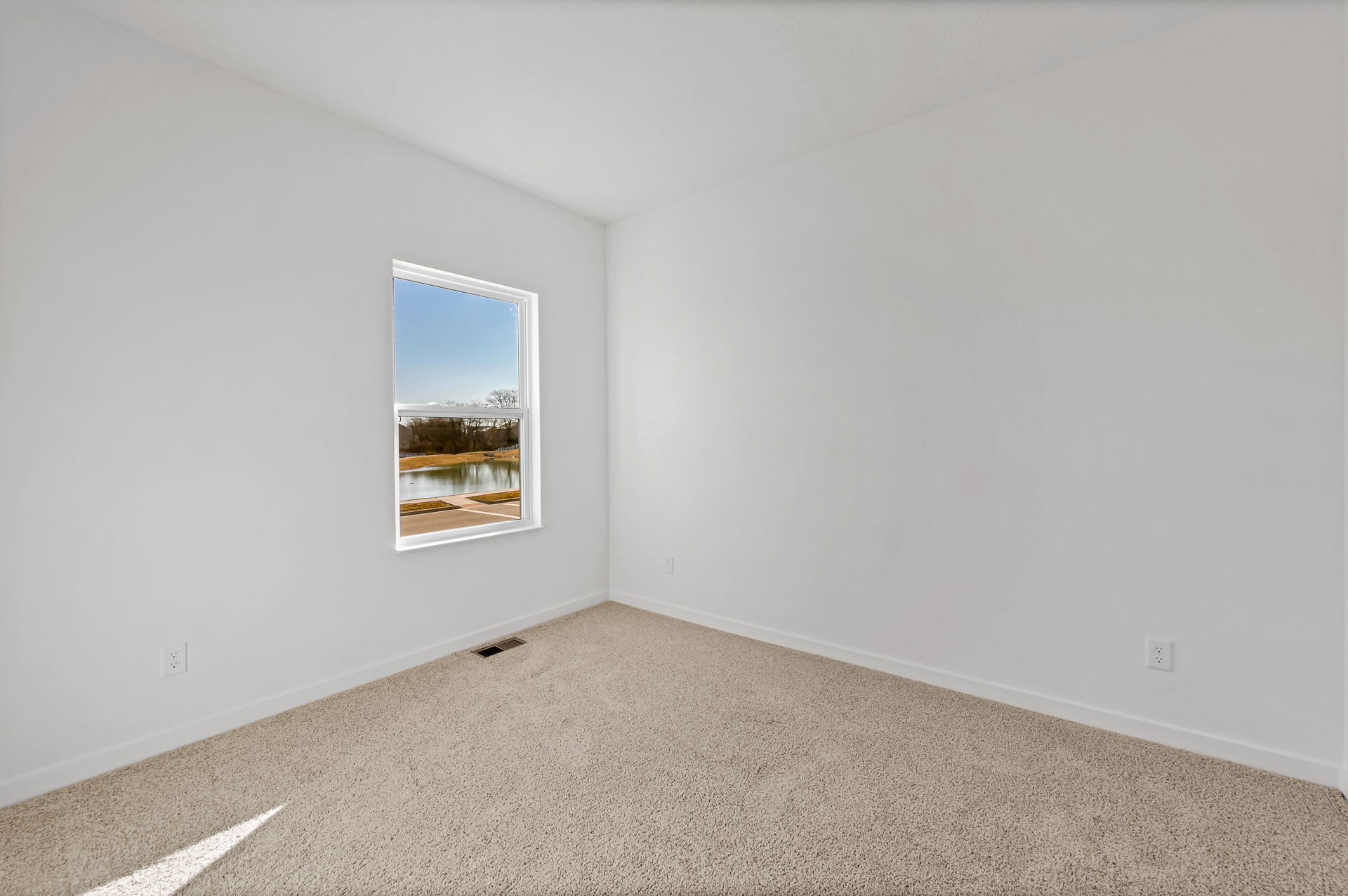A minimalist empty room with beige carpet and a large window overlooking a serene lake view.
